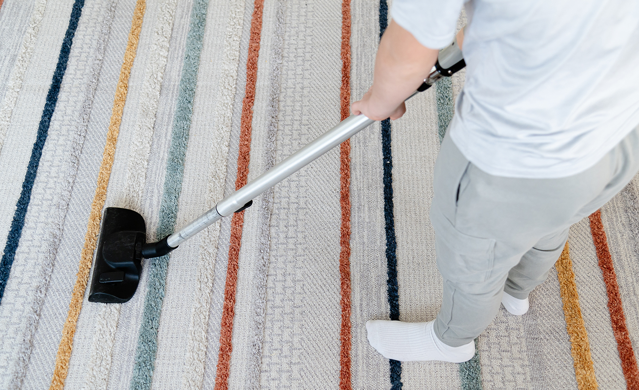 Person vacuuming a rug at home.
