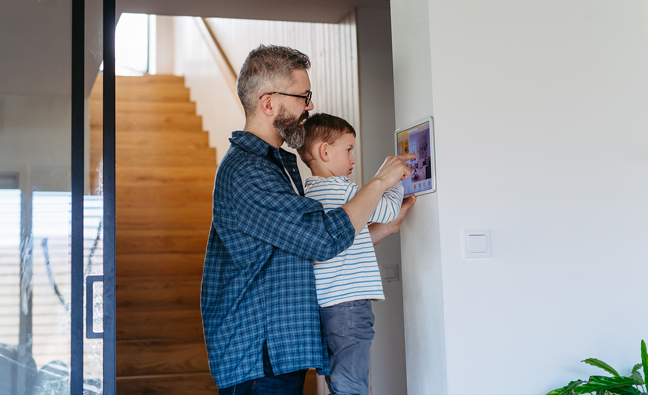 Father and child using a wall-mounted smart home security control panel in a Greenville, SC residence