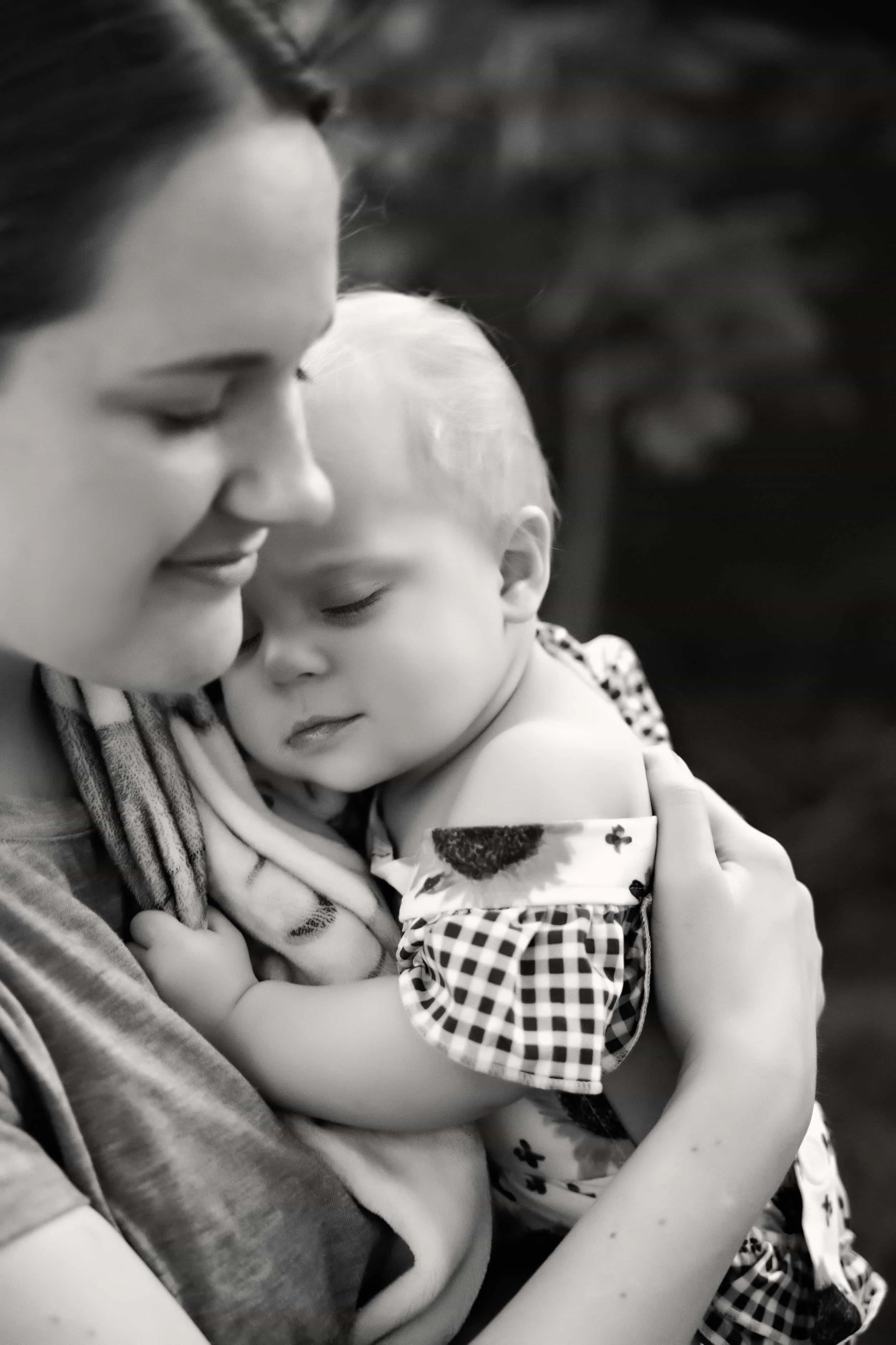 A black and white photo of a woman smiling gently as she holds a young child with closed eyes close to her chest, sharing an intimate tender moment Near Saint Joseph MO.