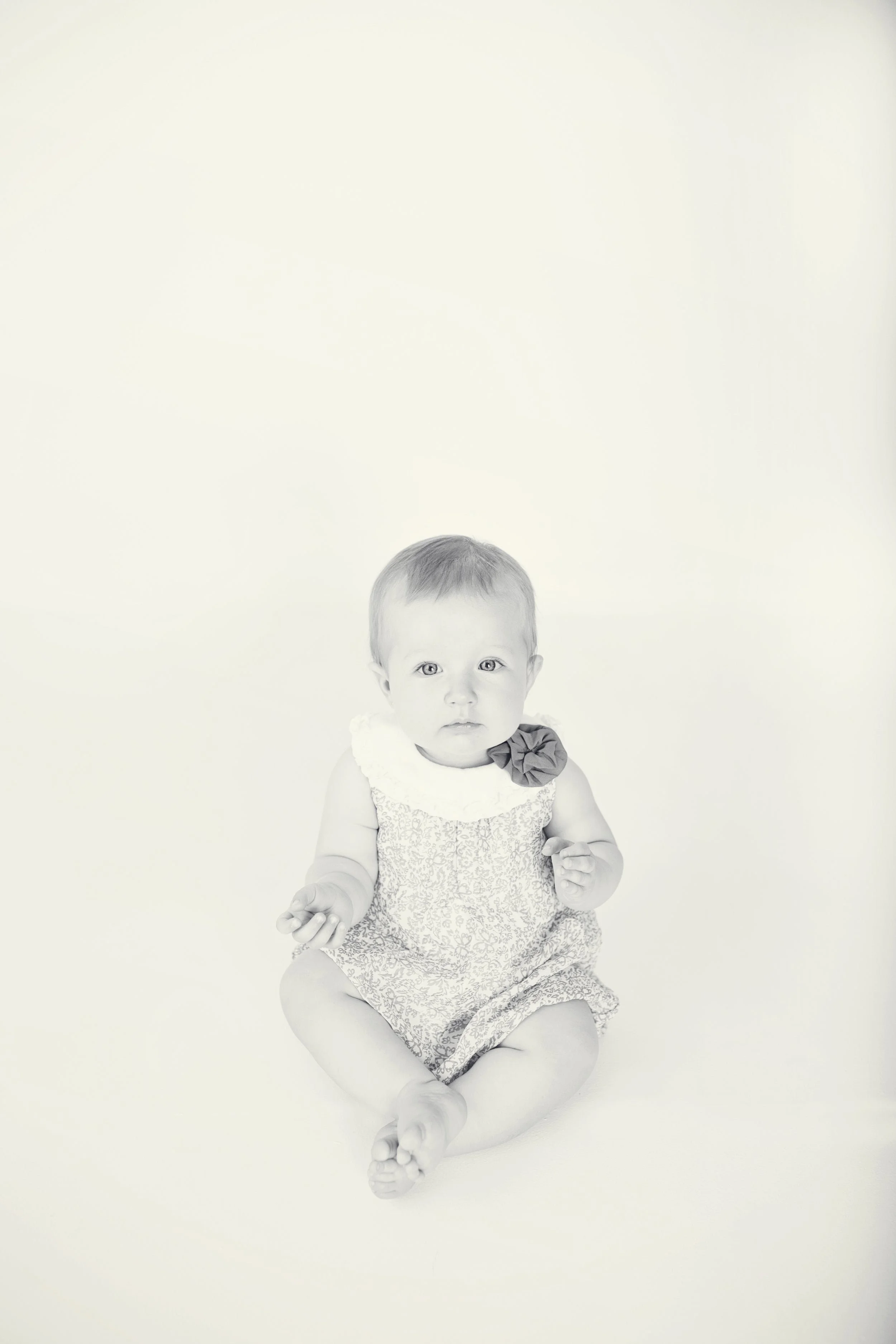 Black and white photo of a young child sitting on the floor, looking directly at the camera, with a plain light background. In Cameron MO