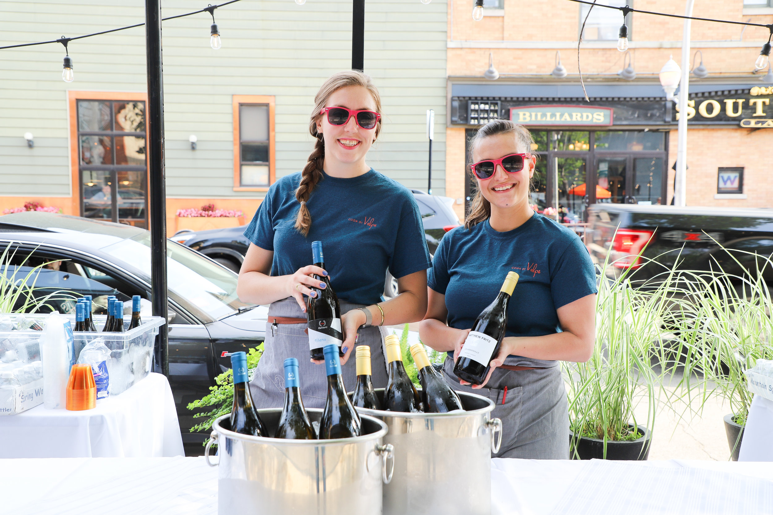 Servers showcase bottles of wine at a Coda di Volpe patio party.