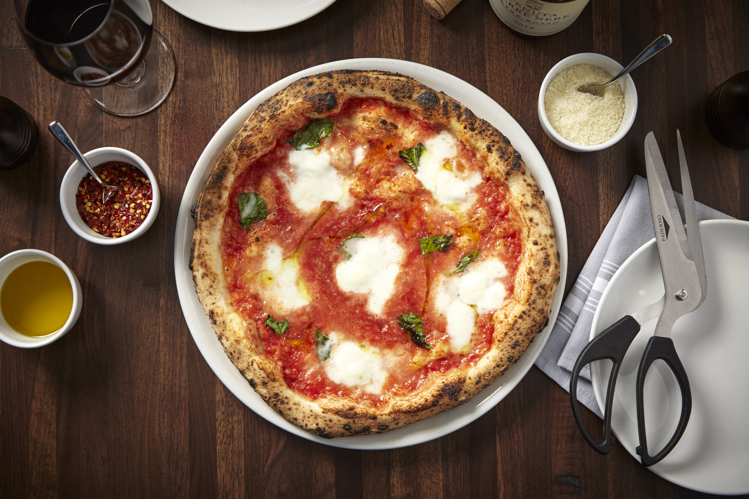 Bird's-eye view showcasing our signature pizza next to a glass of wine and pizza shears.