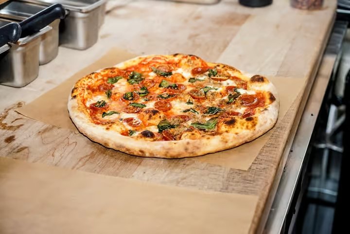Freshly baked pepperoni and basil pizza on parchment paper on a wooden countertop.
