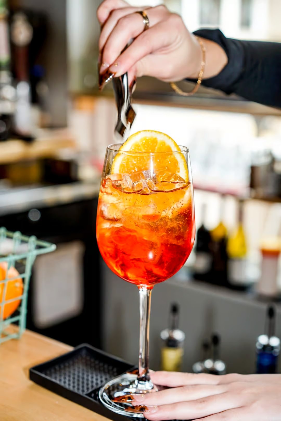 Person preparing a cocktail with orange slice garnish