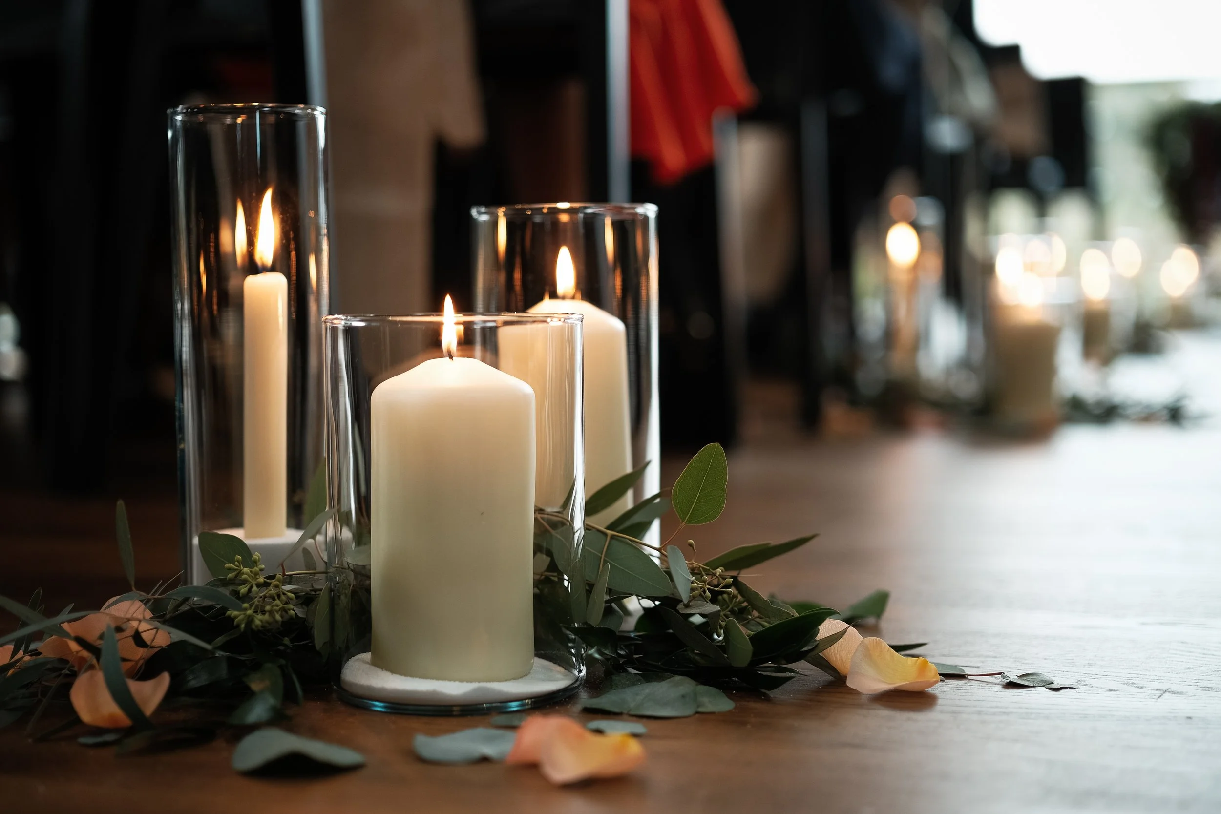 candles lining the aisle of a wedding venue surrounded by eucalyptus and rose petals