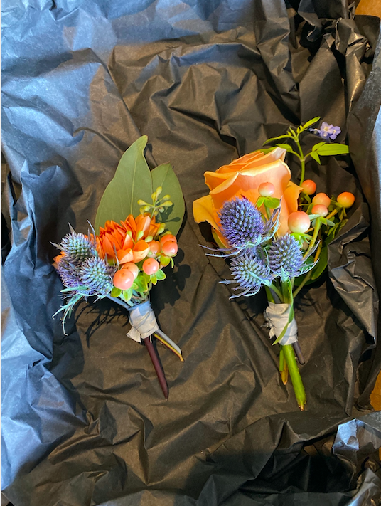 two button holes in peach and blue with dahlia, eryngium, roses and hypericum berries.