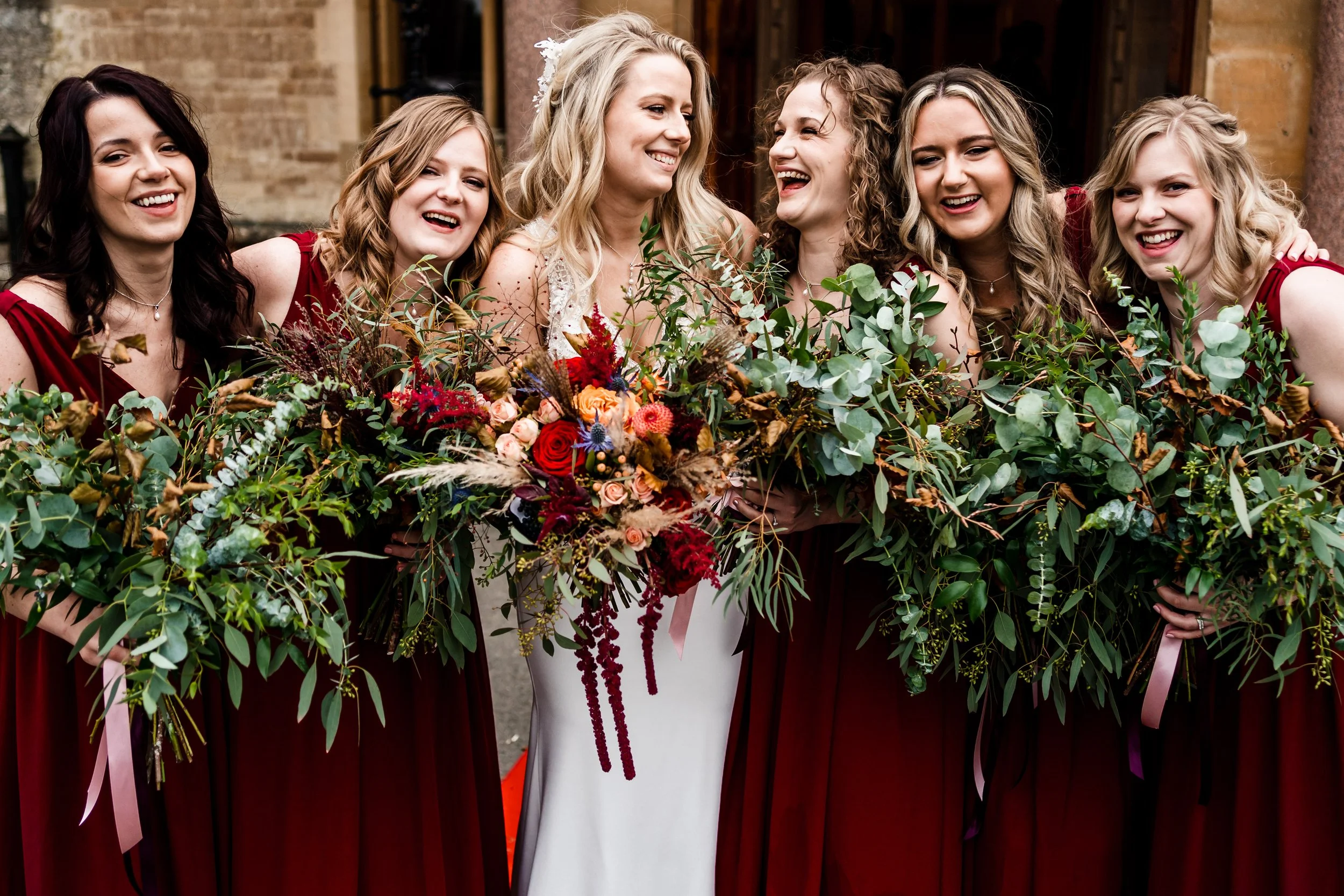 A bride and bridesmaids, the brides bouquet is autumnal deep red and peaches and the bridesmaids bouquets are masses of green foliage