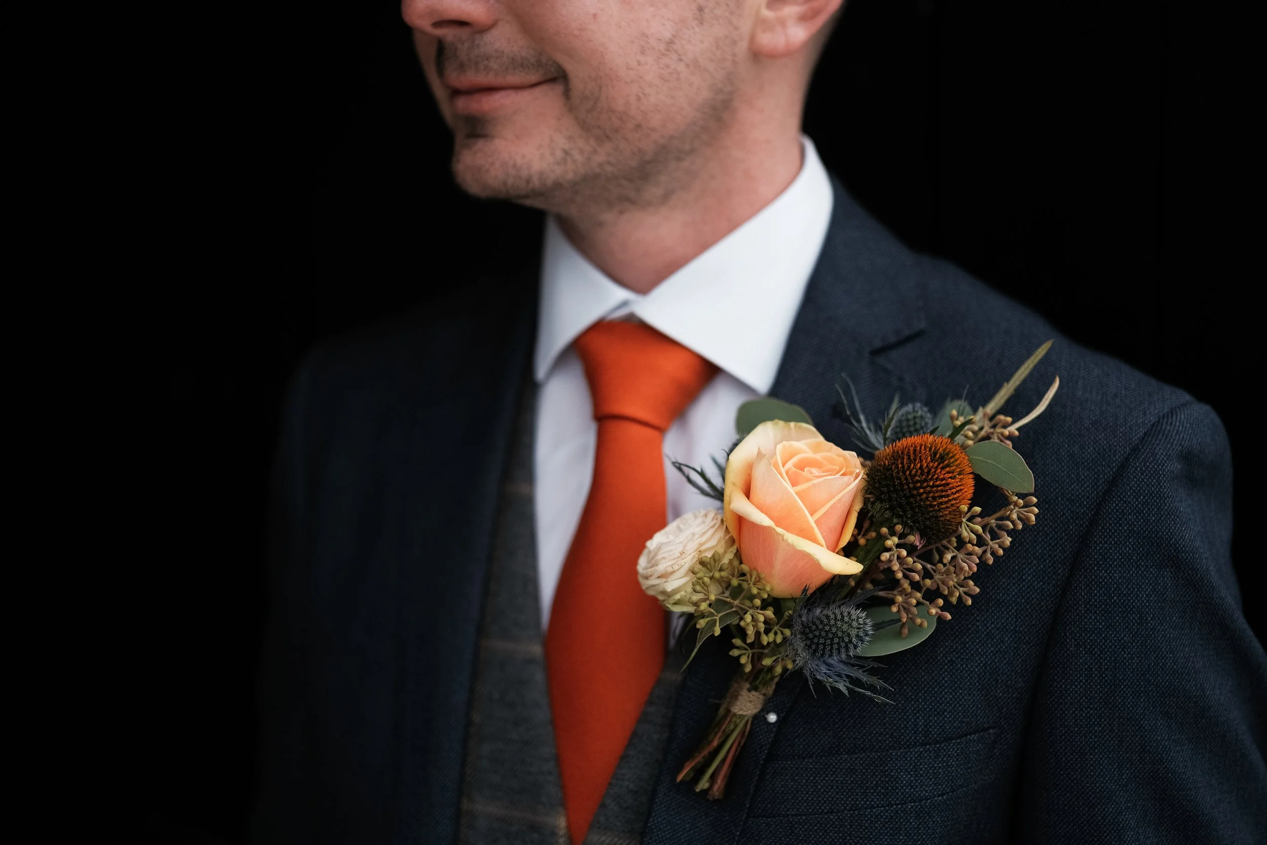 A grooms button hole in autumnal colours containing a rose, Eryngium, Echinacea and Eucalyptus