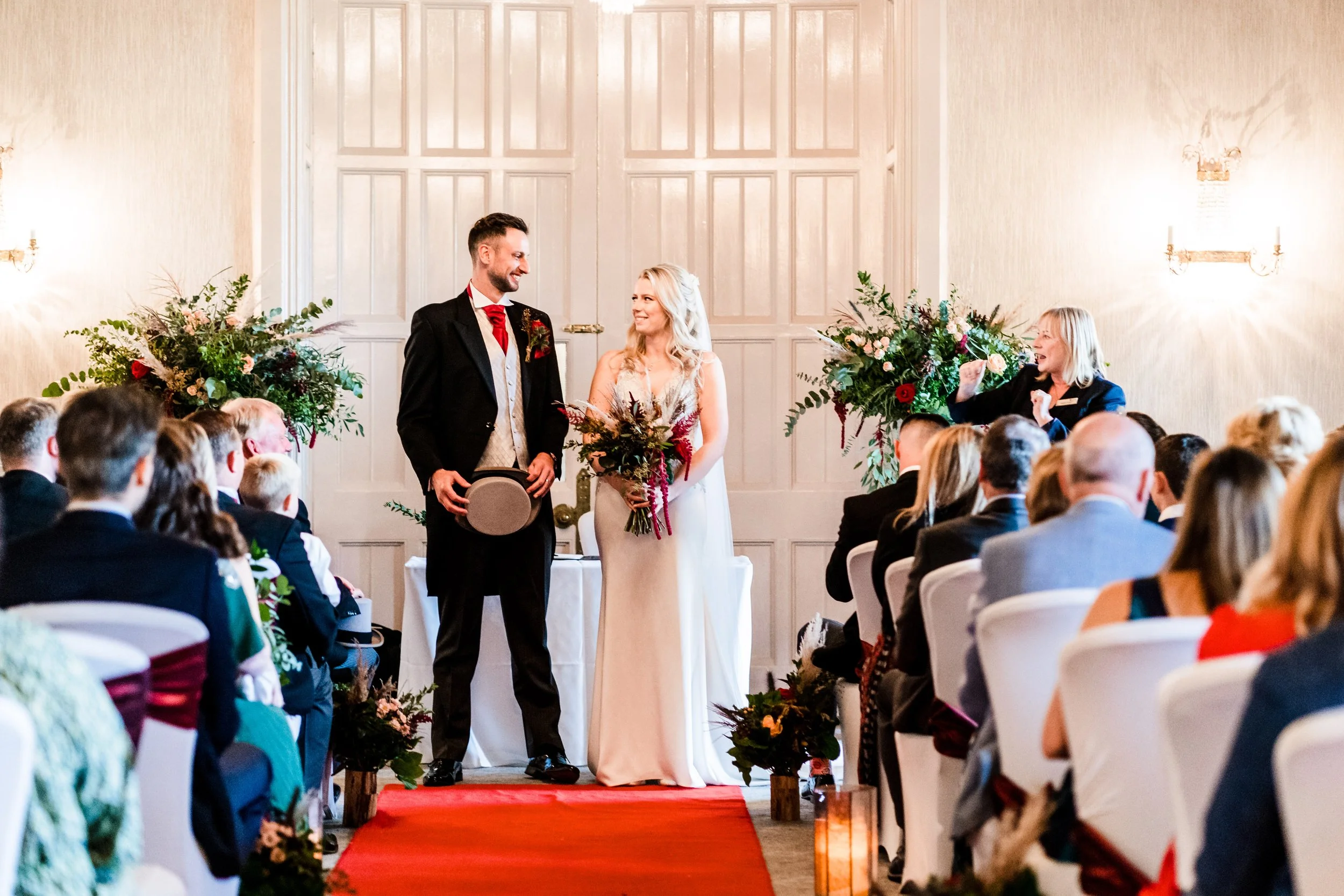 A bride and groom just after they've said their vows. The bride is holding a red autumnal bouquet, there are two urns full of foliage and flowers either side of the couple.