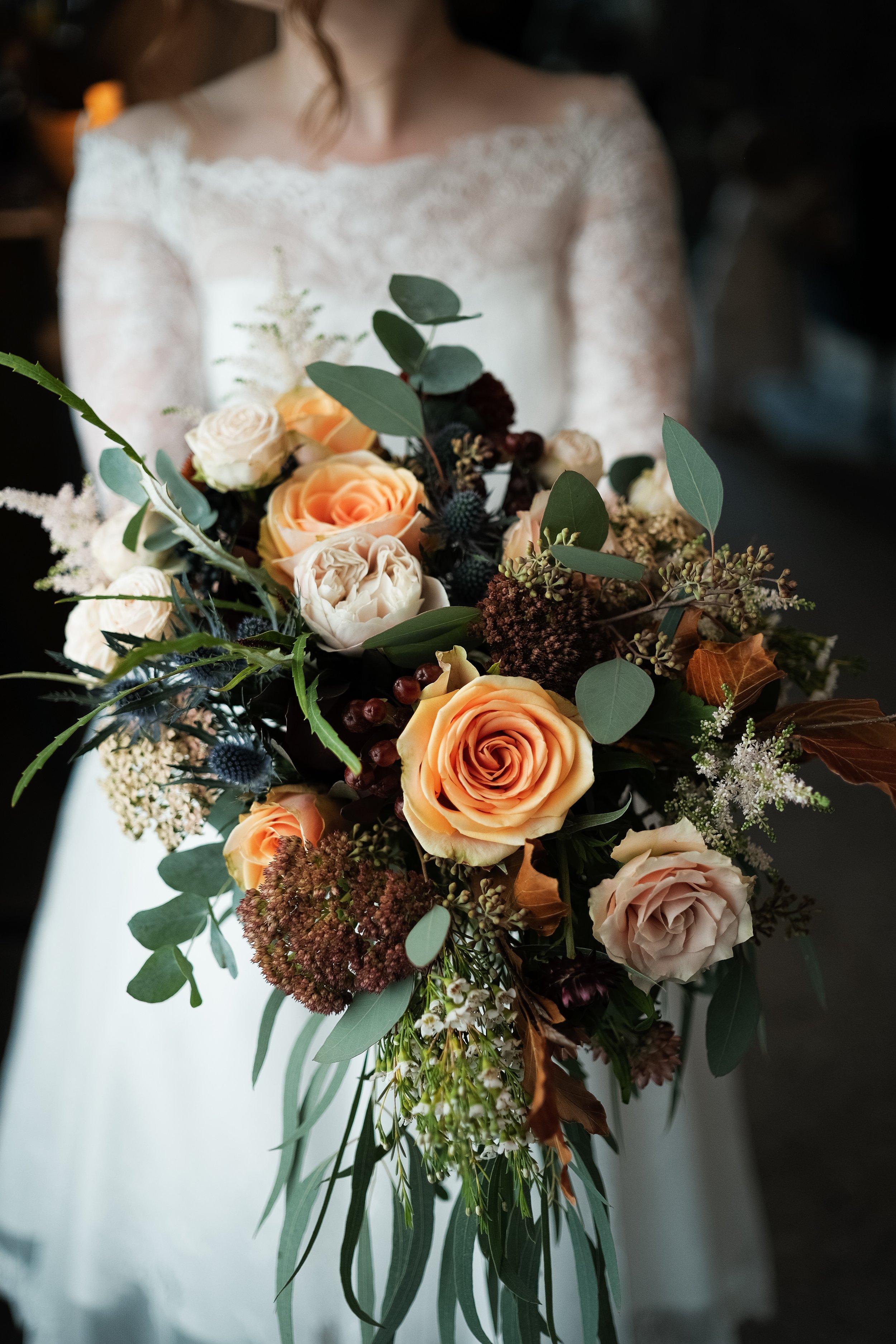 A bridal bouquet in peaches and autumnal colours containing roses, Sedum, Eryngium, Astilbe, Eucalyptus, copper beech leaves.