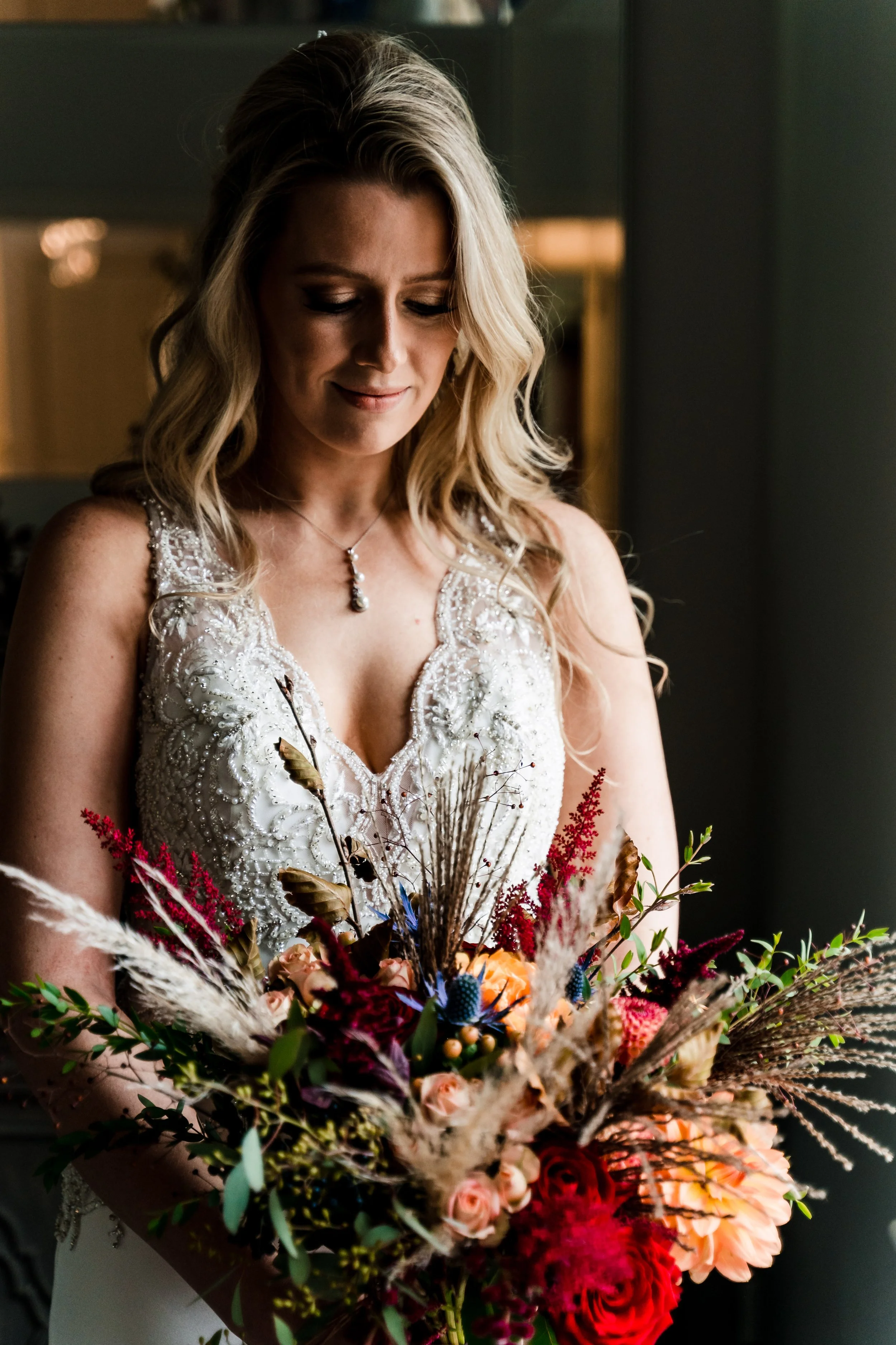 A bride with her bouquet in deep red autumnal colours containing roses, eryngium, pampas, eucalyptus, astilbe, copper beech, amaranth, dahlia, miscanthus.