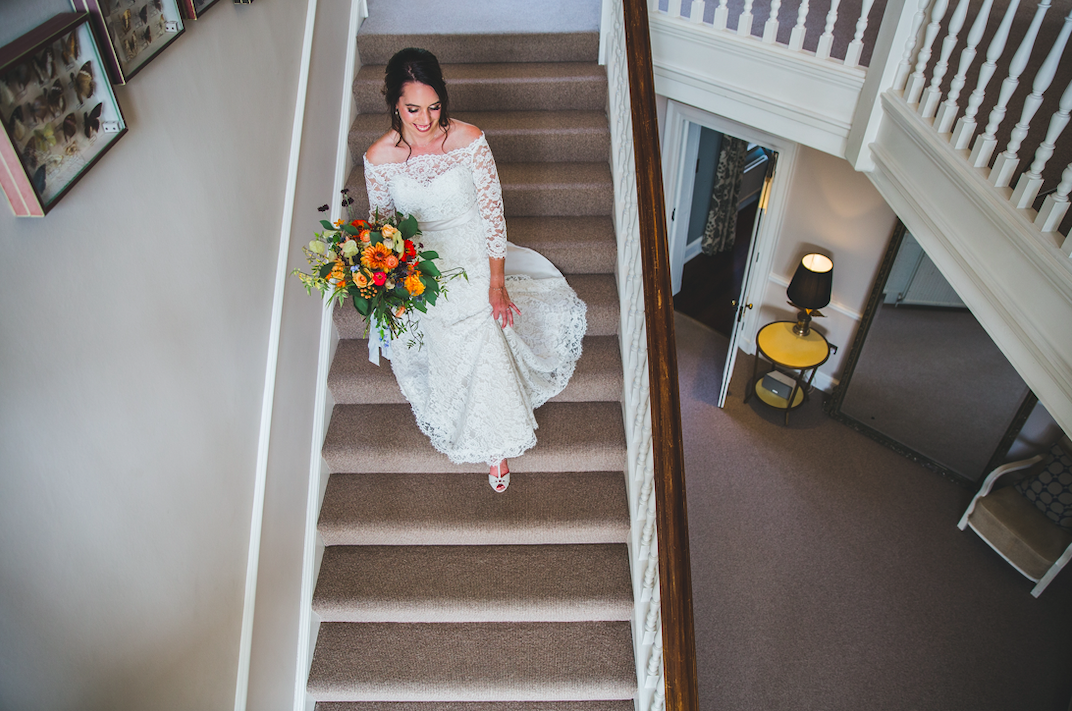 a bride walking downstairs holding a bouquet in rich autumn colours
