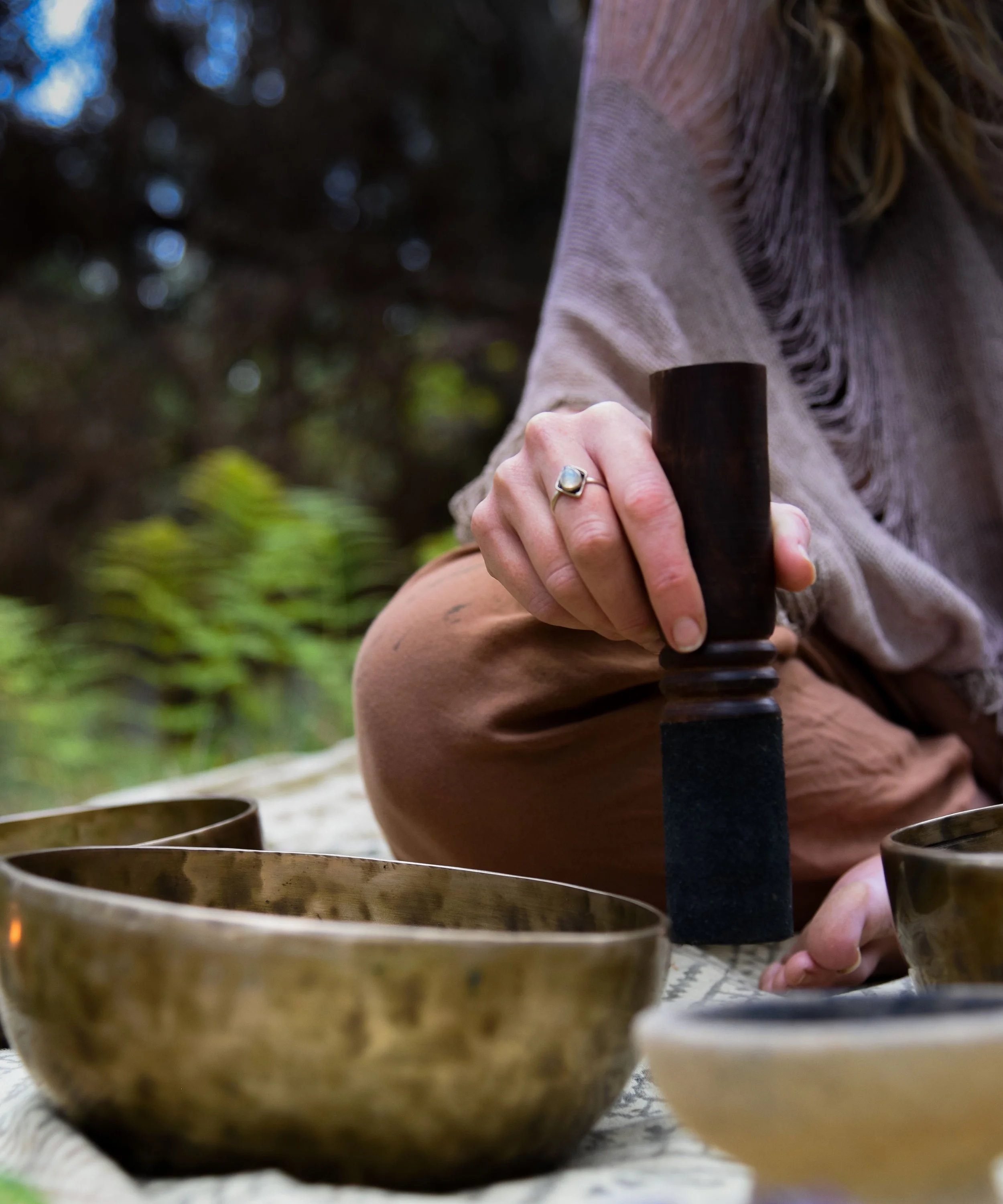 Person using a striker to produce sound on Tibetan singing bowls outdoors.