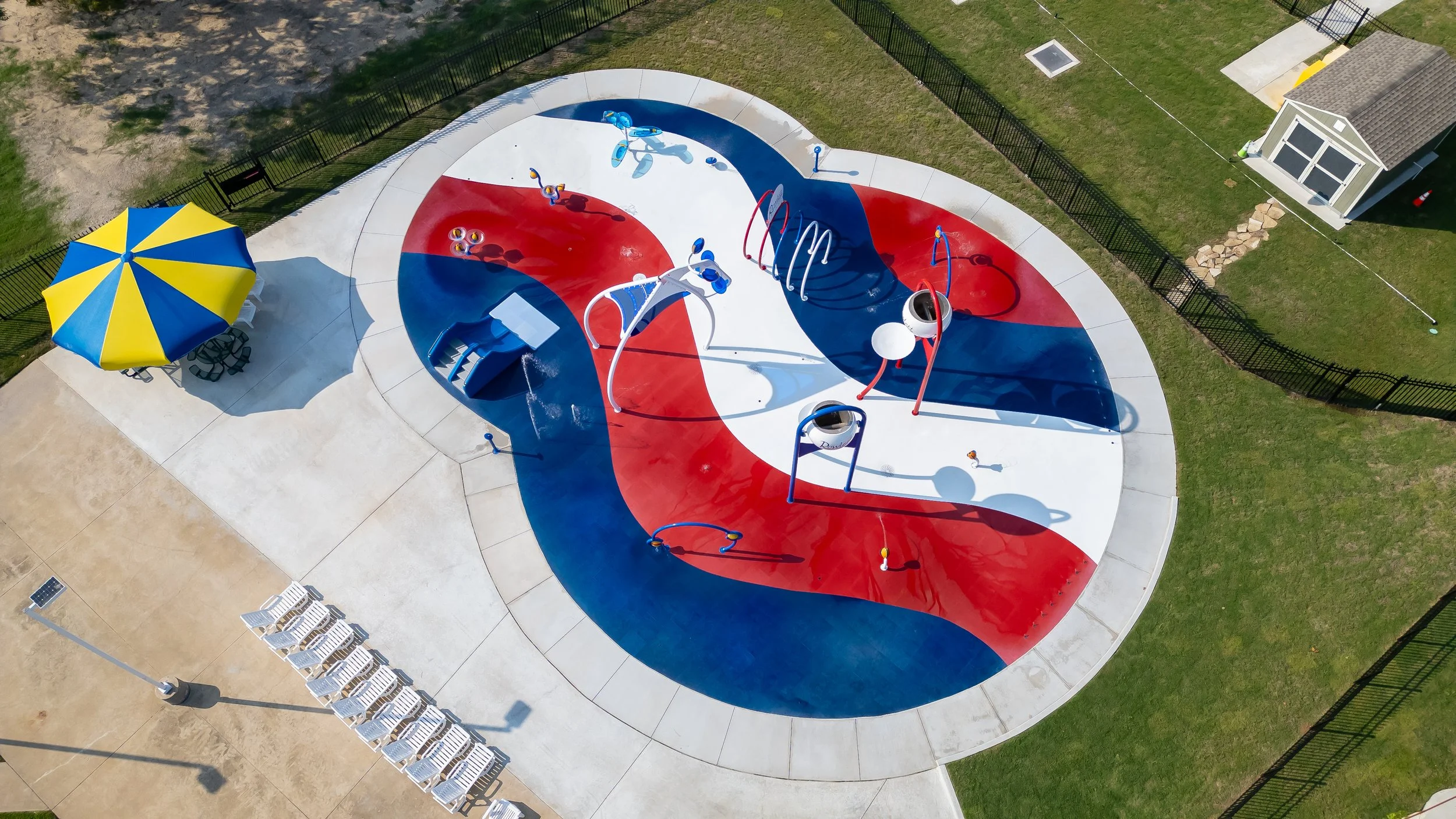 Red, white, and blue Life Floor splash pad surfacing curves across Wet Zone Waterpark in Rowlett, Texas.