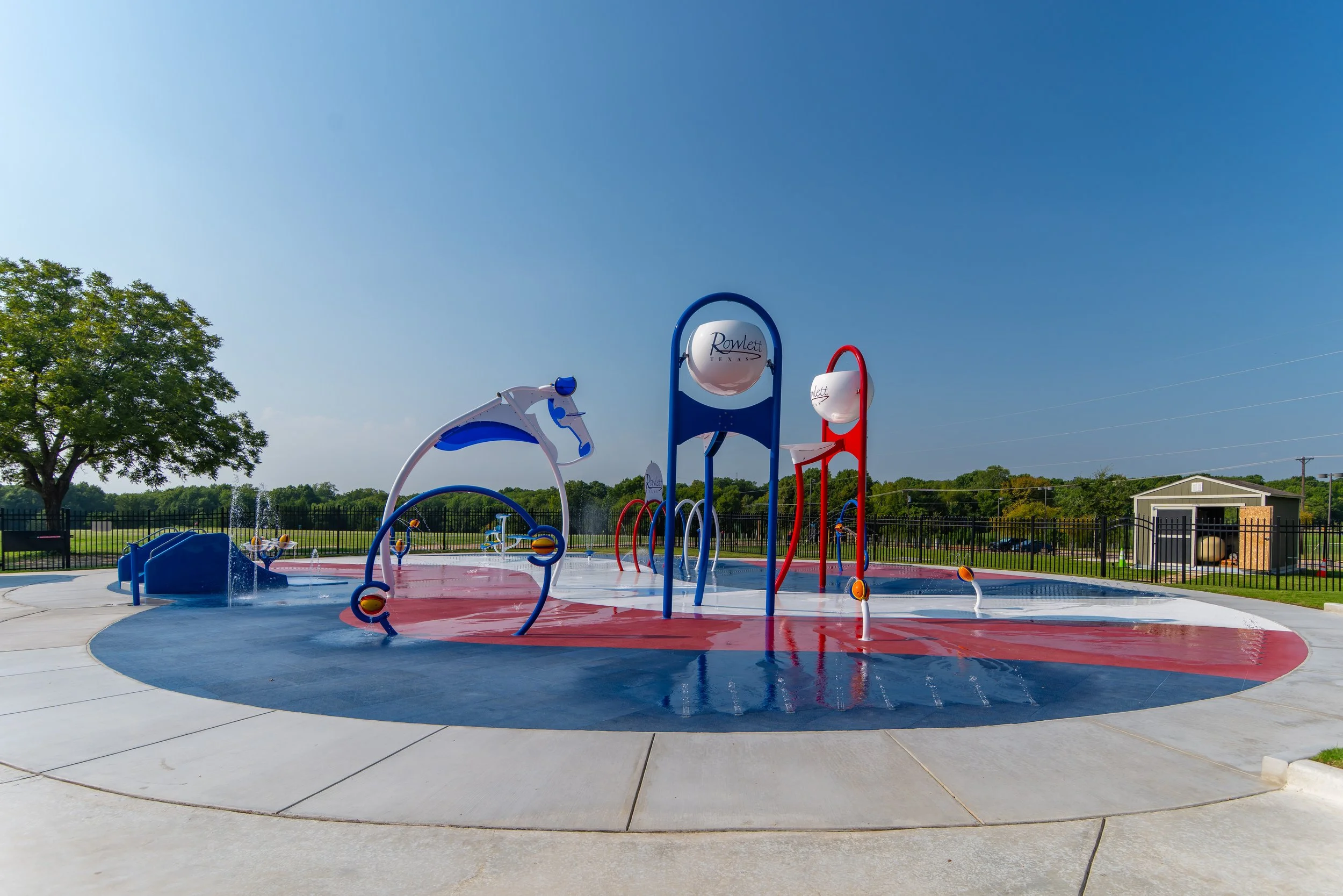 Red, white, and blue Life Floor splash pad surfacing curves across Wet Zone Waterpark in Rowlett, Texas.