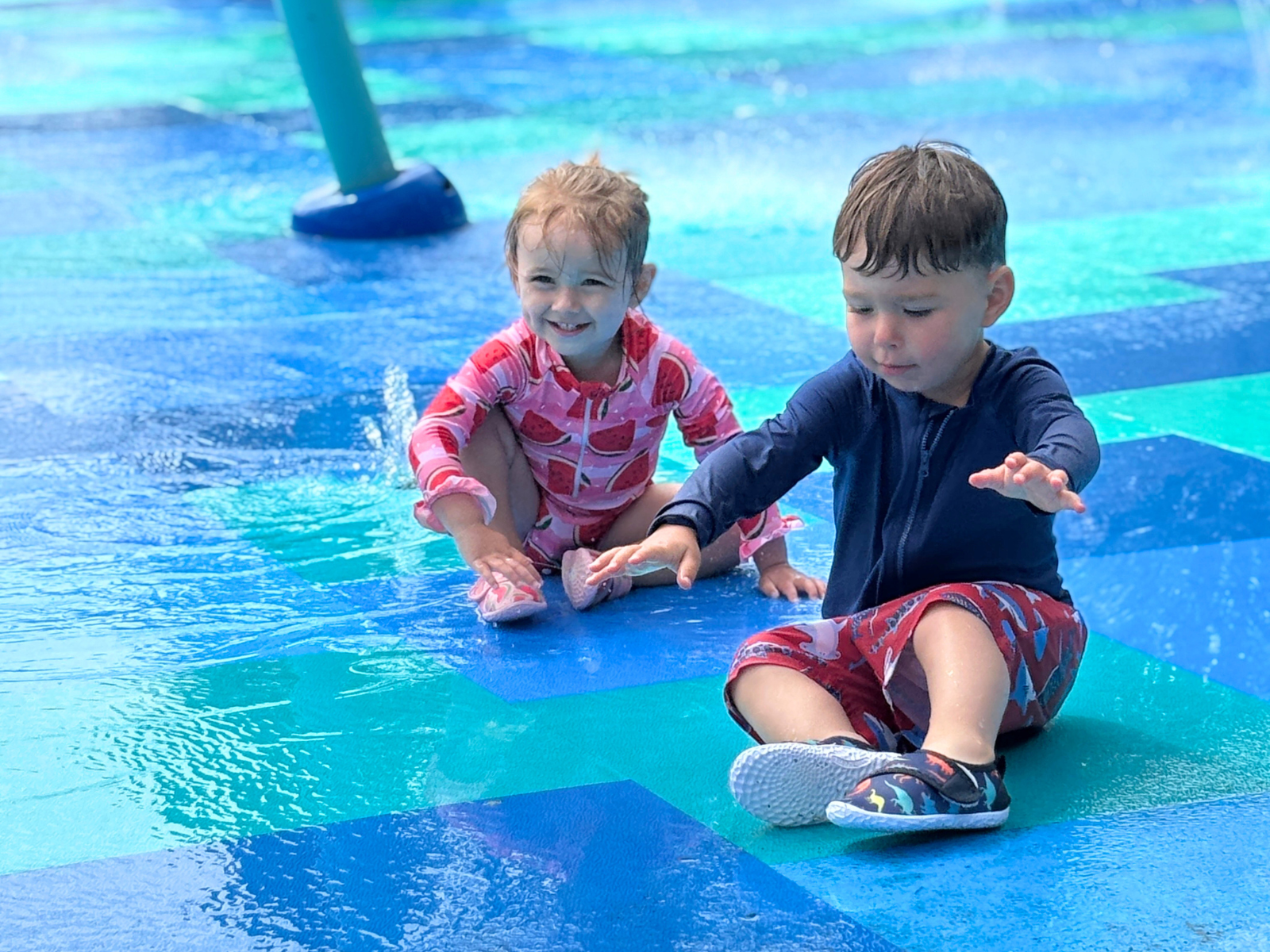 Two children sitting on Life Floor splash pad with safety surfacing.