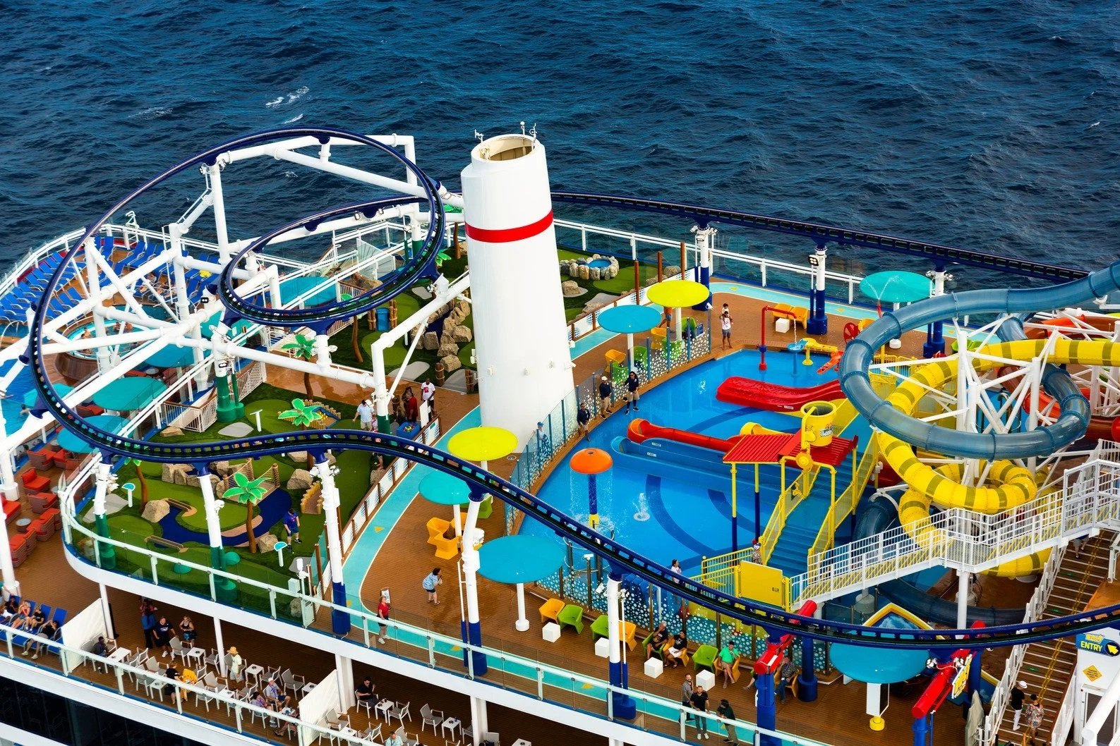 Carnival's Mardi Gras water play zone with Life Floor aquatic safety surfacing among people, slides, and sea coaster