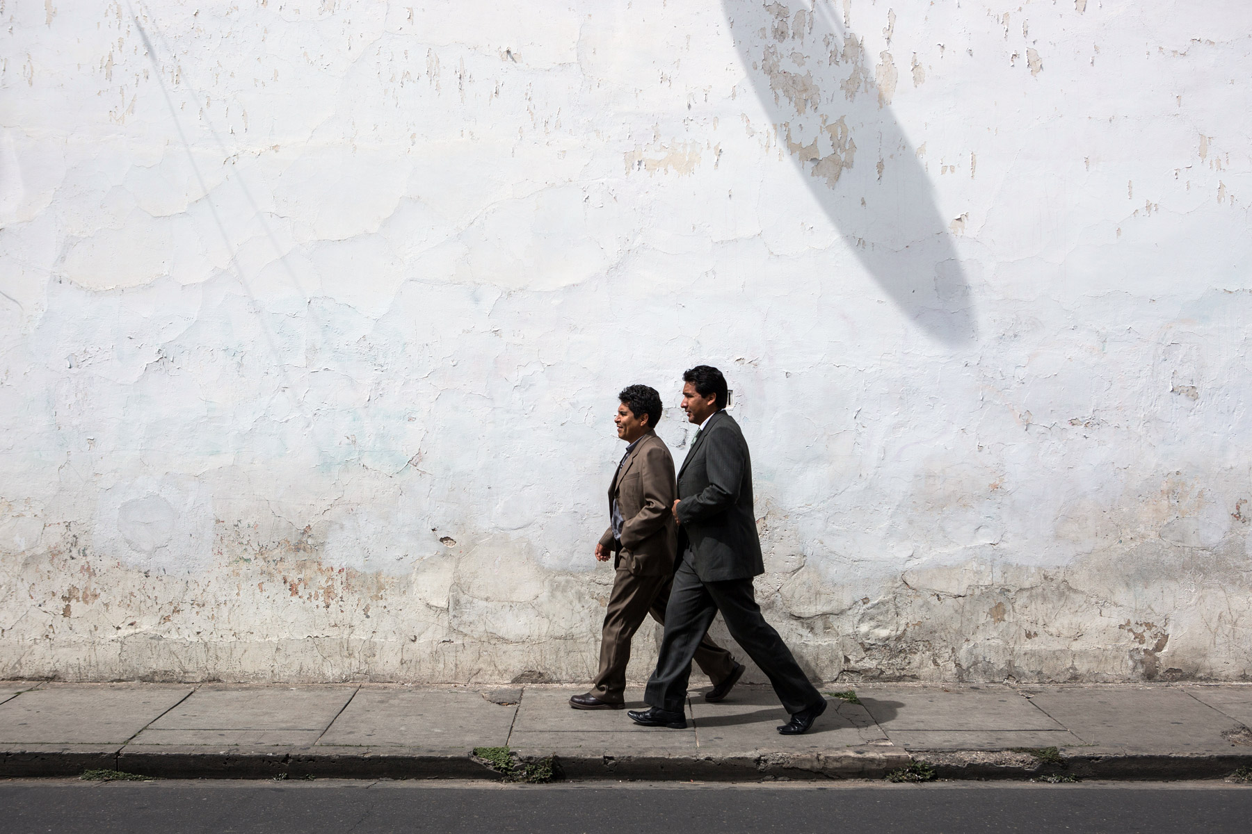 2 men walking in front of a white wall in Sucre, Bolivia