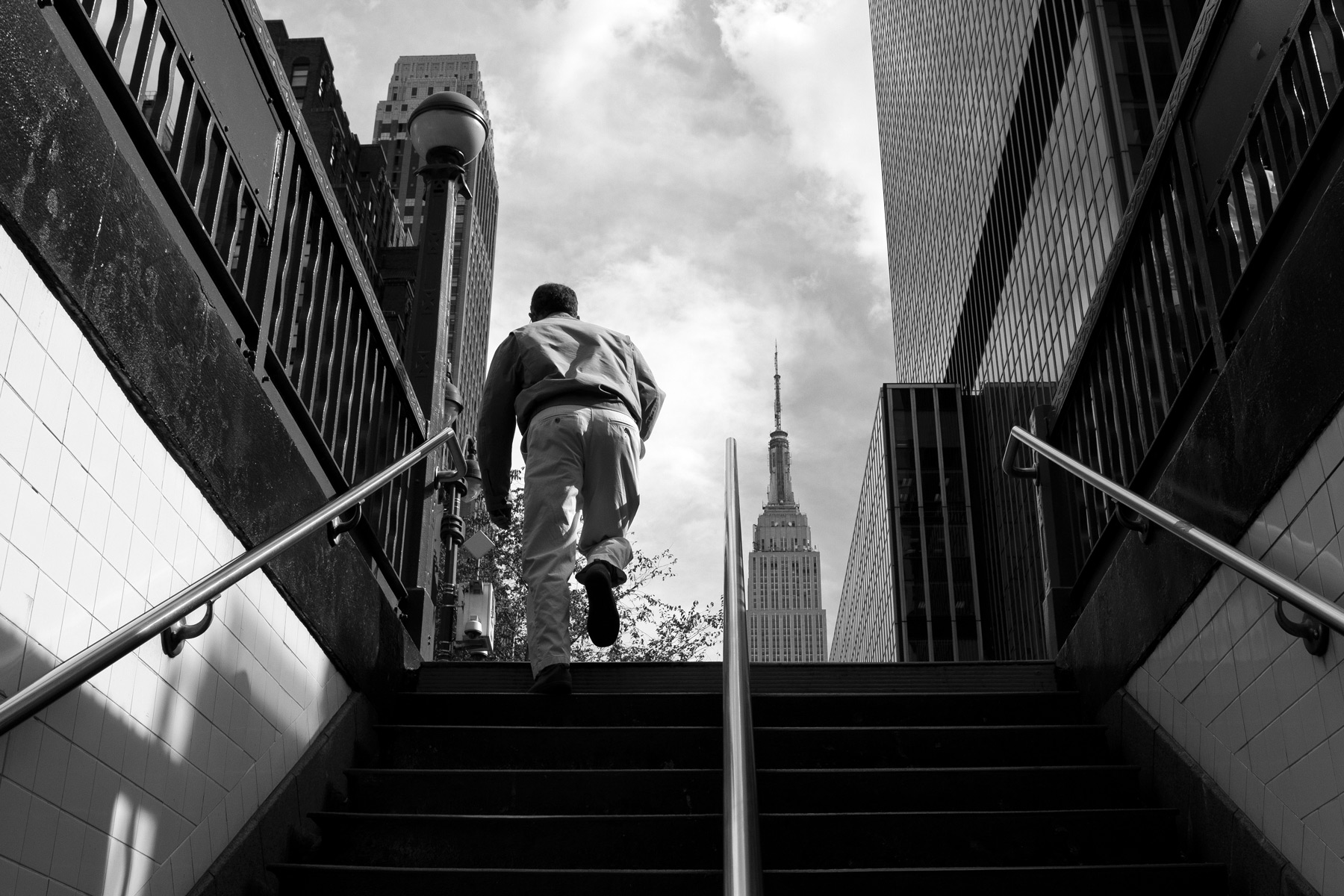 A man walking up stairs from the subway with the Empire State building in the background