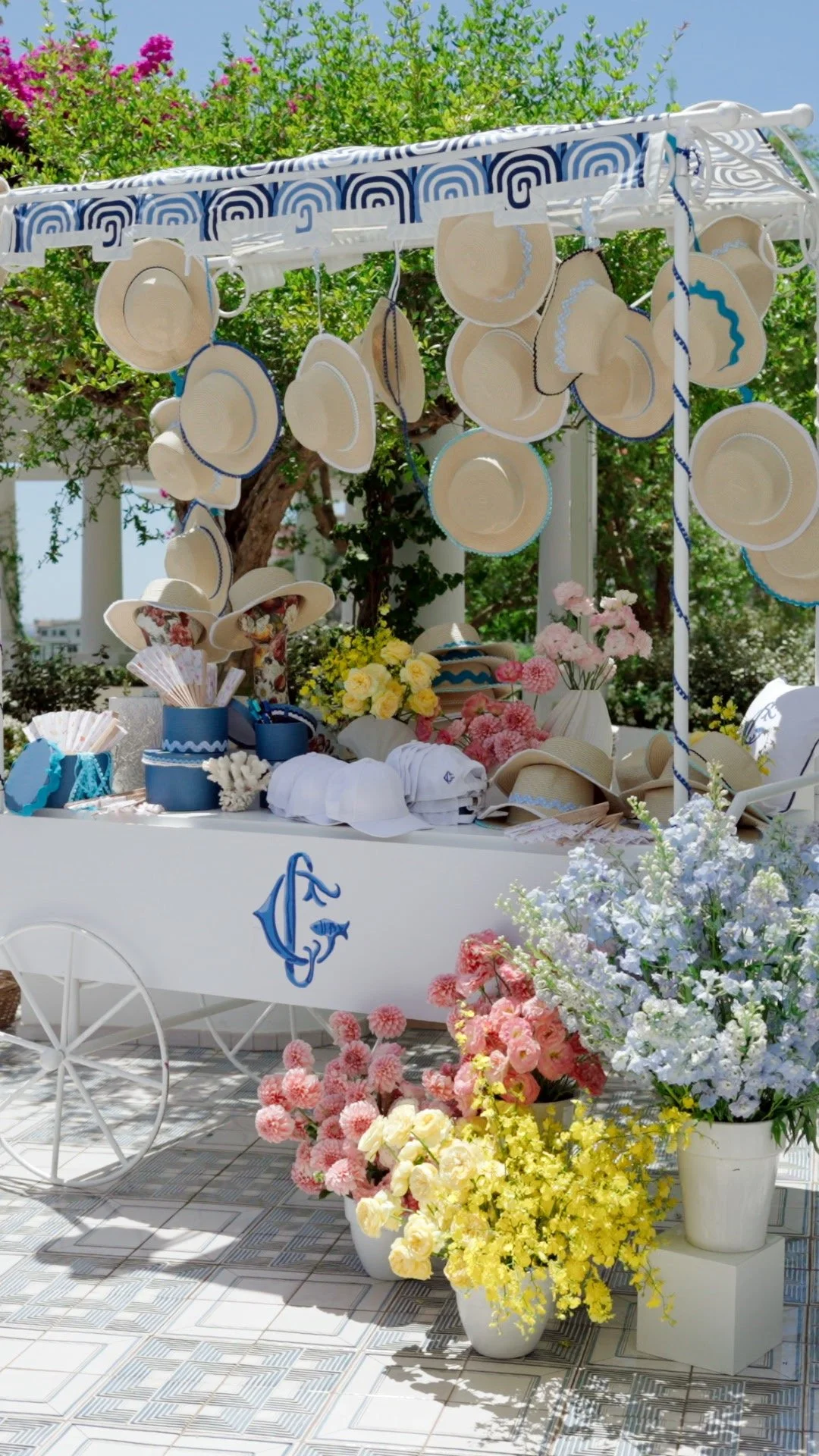 Display of summer hats, parasols, and flowers at an outdoor market or event setup.