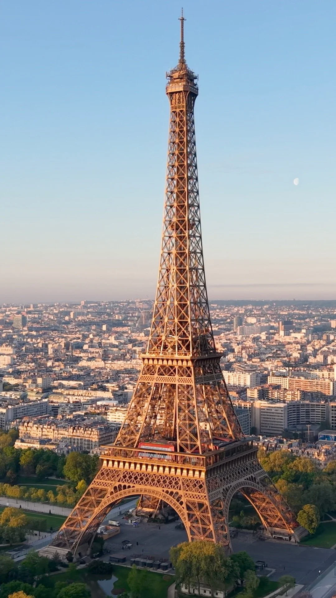 Tall Eiffel Tower in Paris with cityscape and moon in the background, taken during sunset.