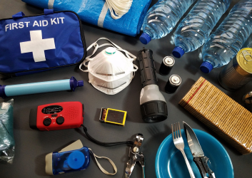 Emergency supplies, including first aid kit, bottled water, battery-powered radio, and canned food, used in an example of a hurricane supply kit