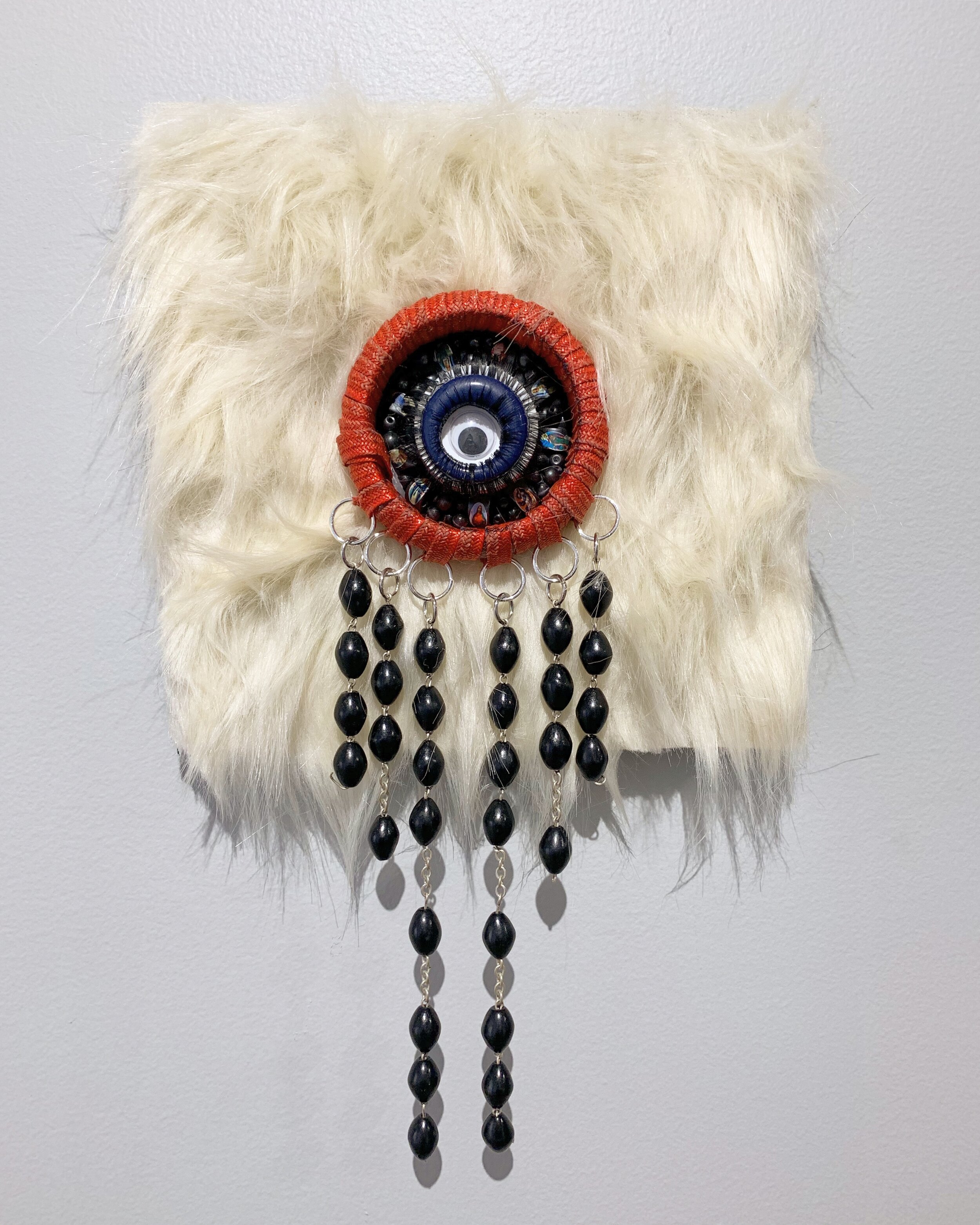   Eye of Providence,  2020, faux fur, costume jewelry, beads, and a googley eye on panel, 8x8” 