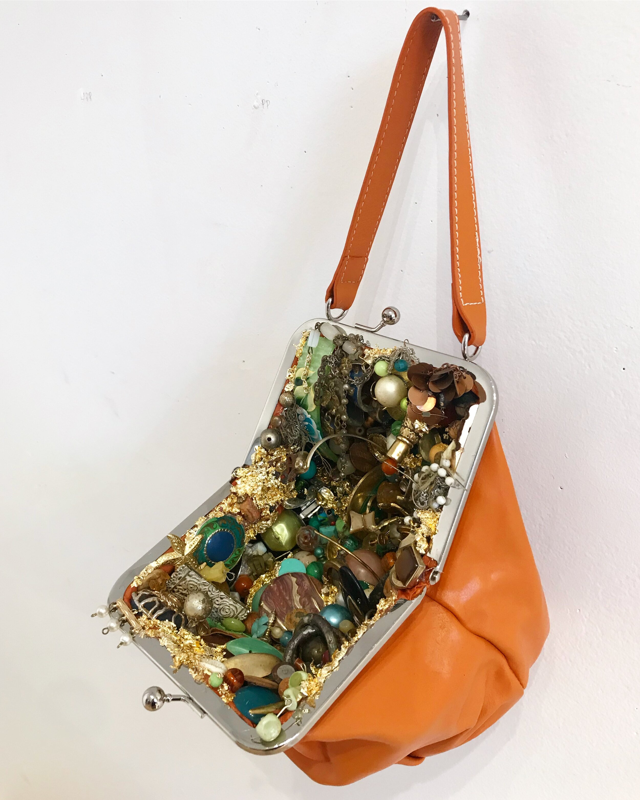   Orange Bag,  2019, costume jewelry, gold leaf, beads, and dirt in orange purse, 9x13”  