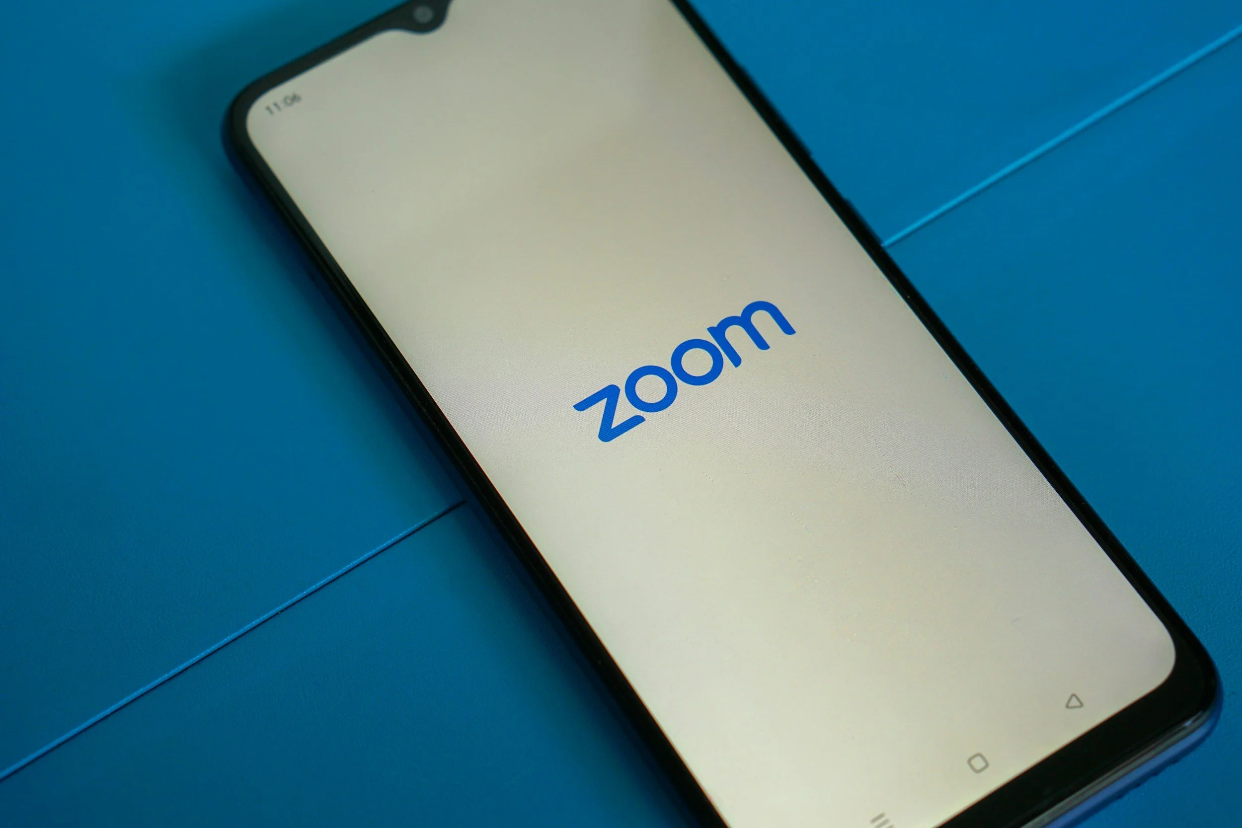 A smartphone displaying the Zoom logo on the screen, placed on a blue surface.