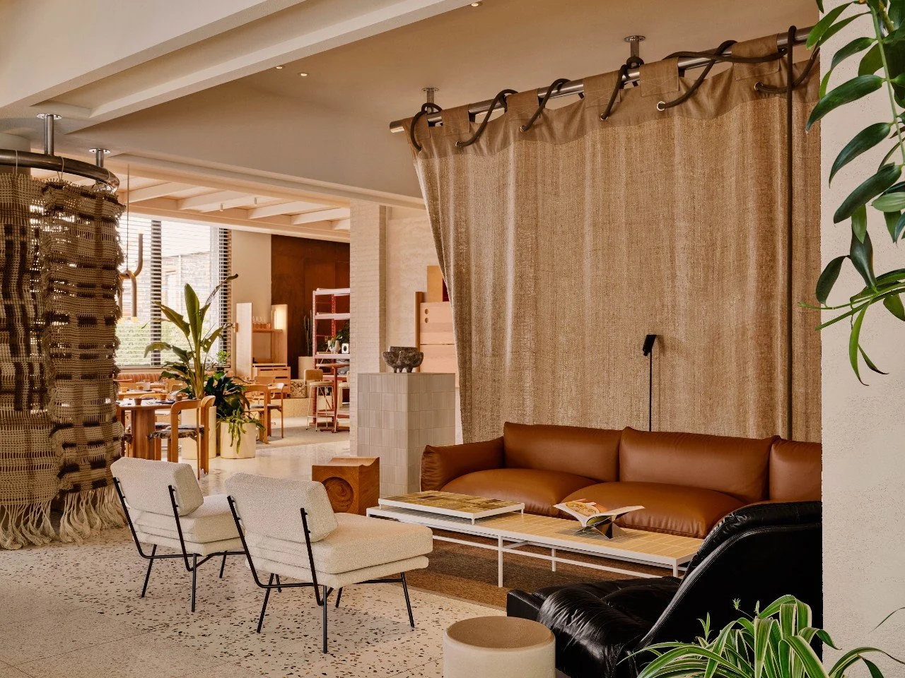 A lounge space with white chairs and brown sofa with a neutral coloured curtain behind..
