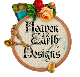 Cross-stitch embroidery with the phrase 'Heaven and Earth Designs' and floral accents, including roses, a top hat, a gold key, a miniature umbrella, and a small golden bell.