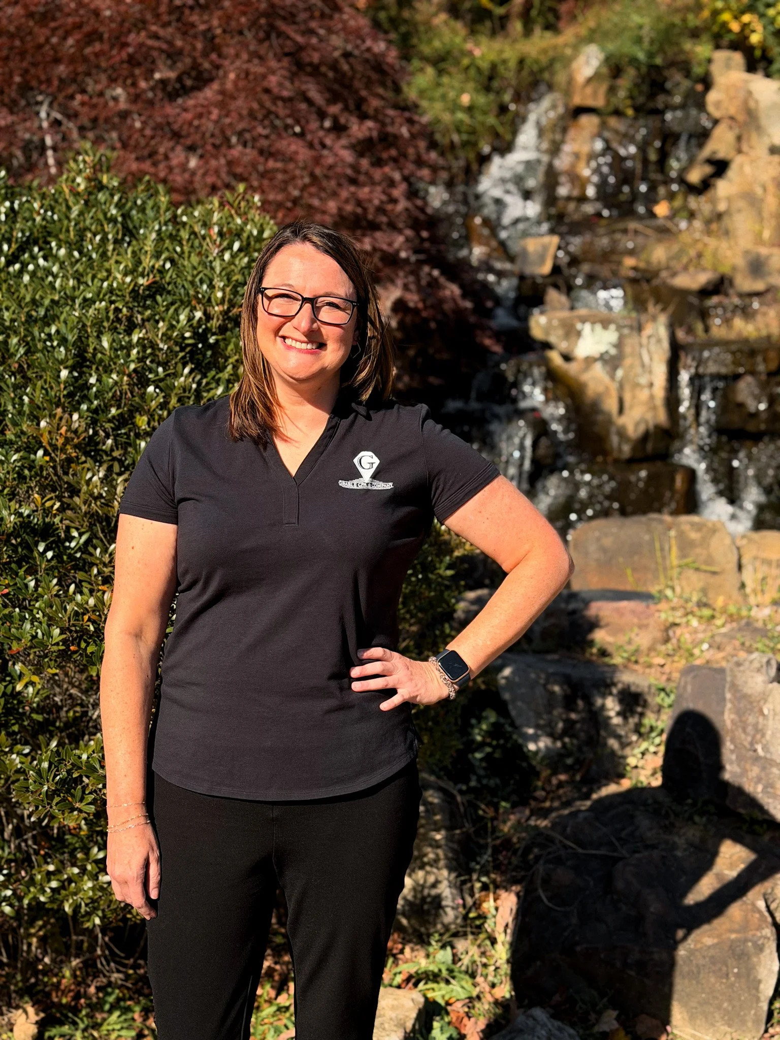 Woman with brown hair, glasses, and a striped sweater smiling against a neutral wall.