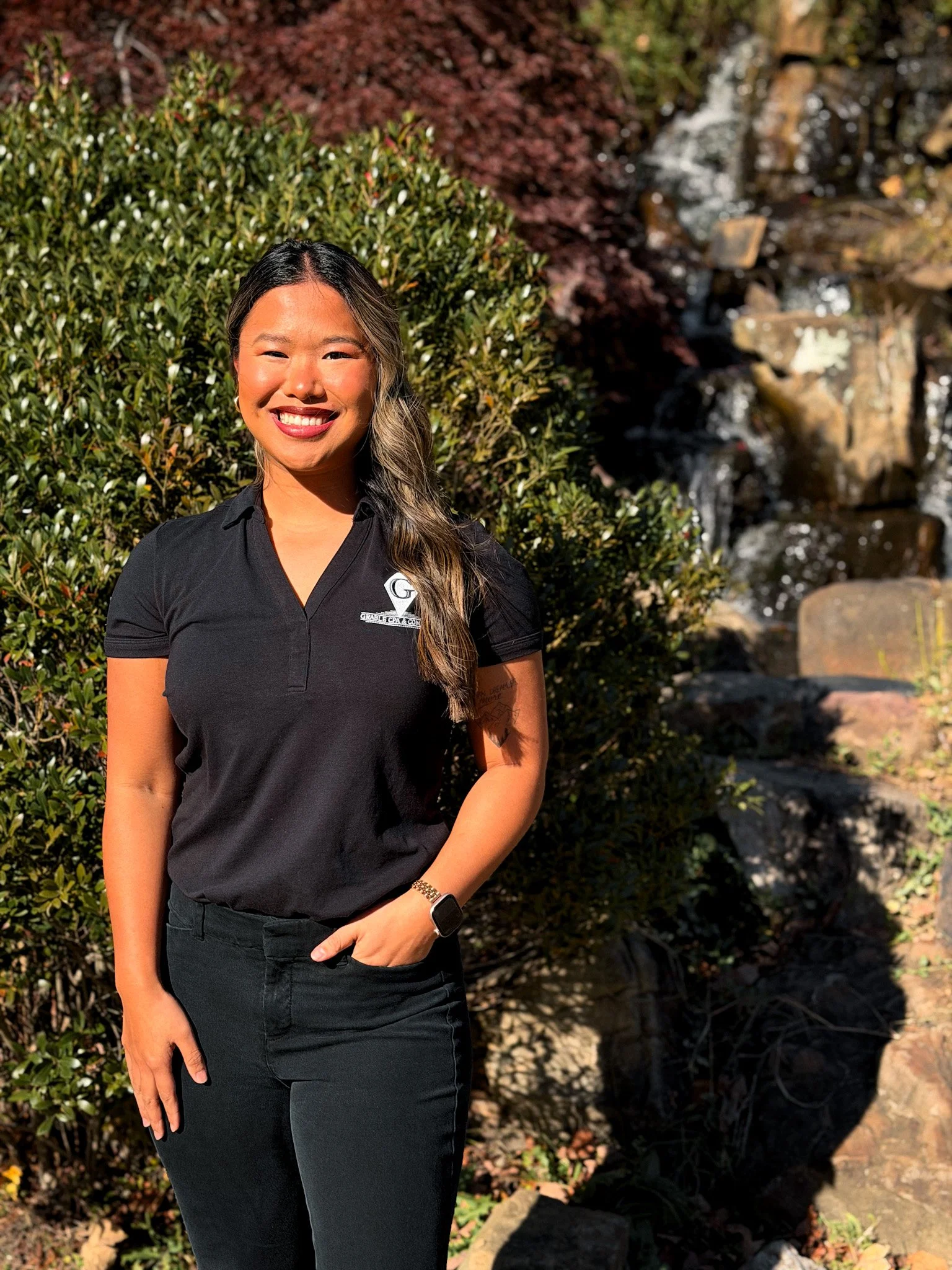 A young woman with long, straight, light brown hair smiling in front of a plain light-colored wall.