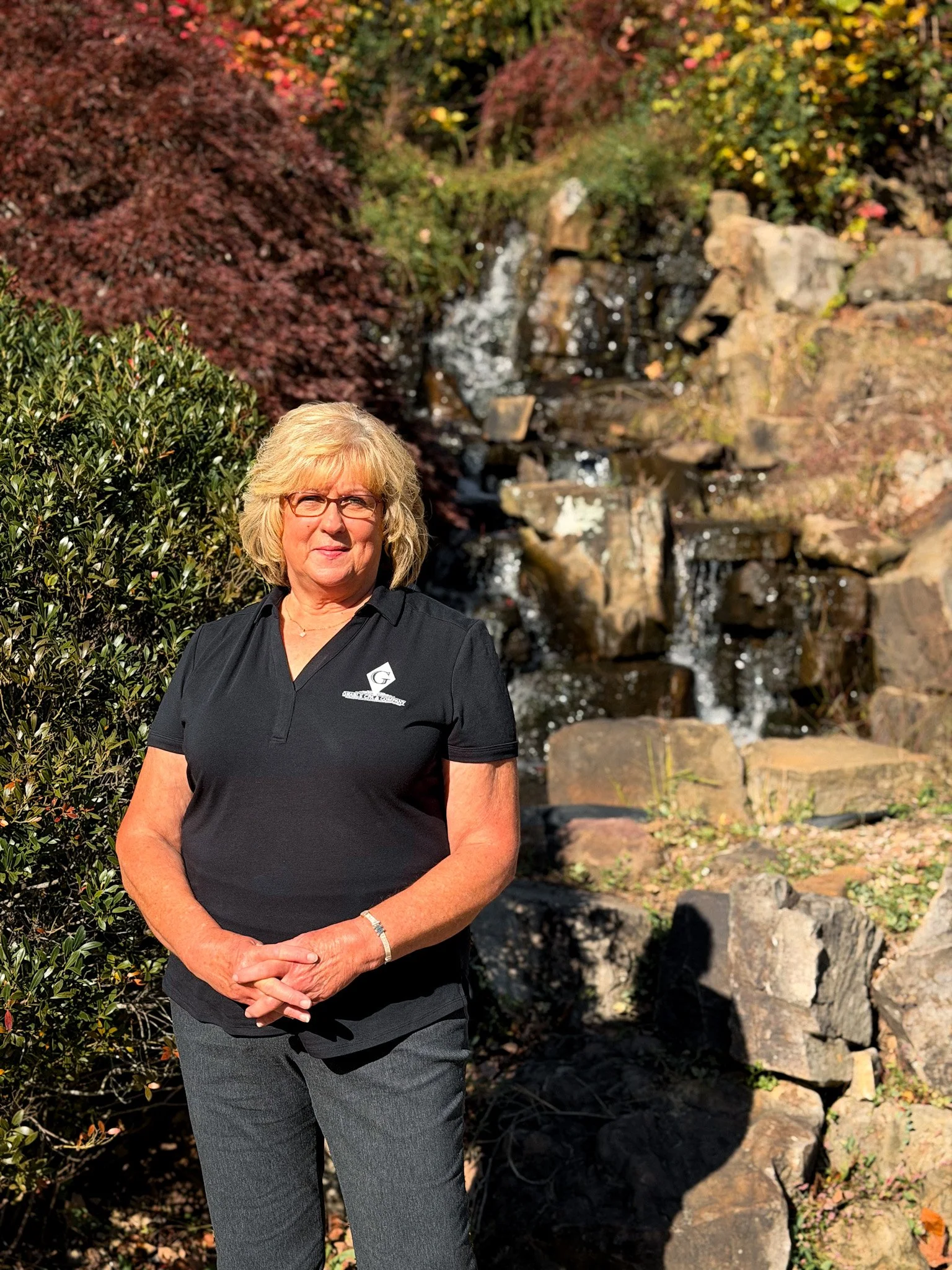 A woman with blonde hair, glasses, and wearing a red button-up shirt standing next to a door with a sign that reads 'Cody L. Grable, CPA'.