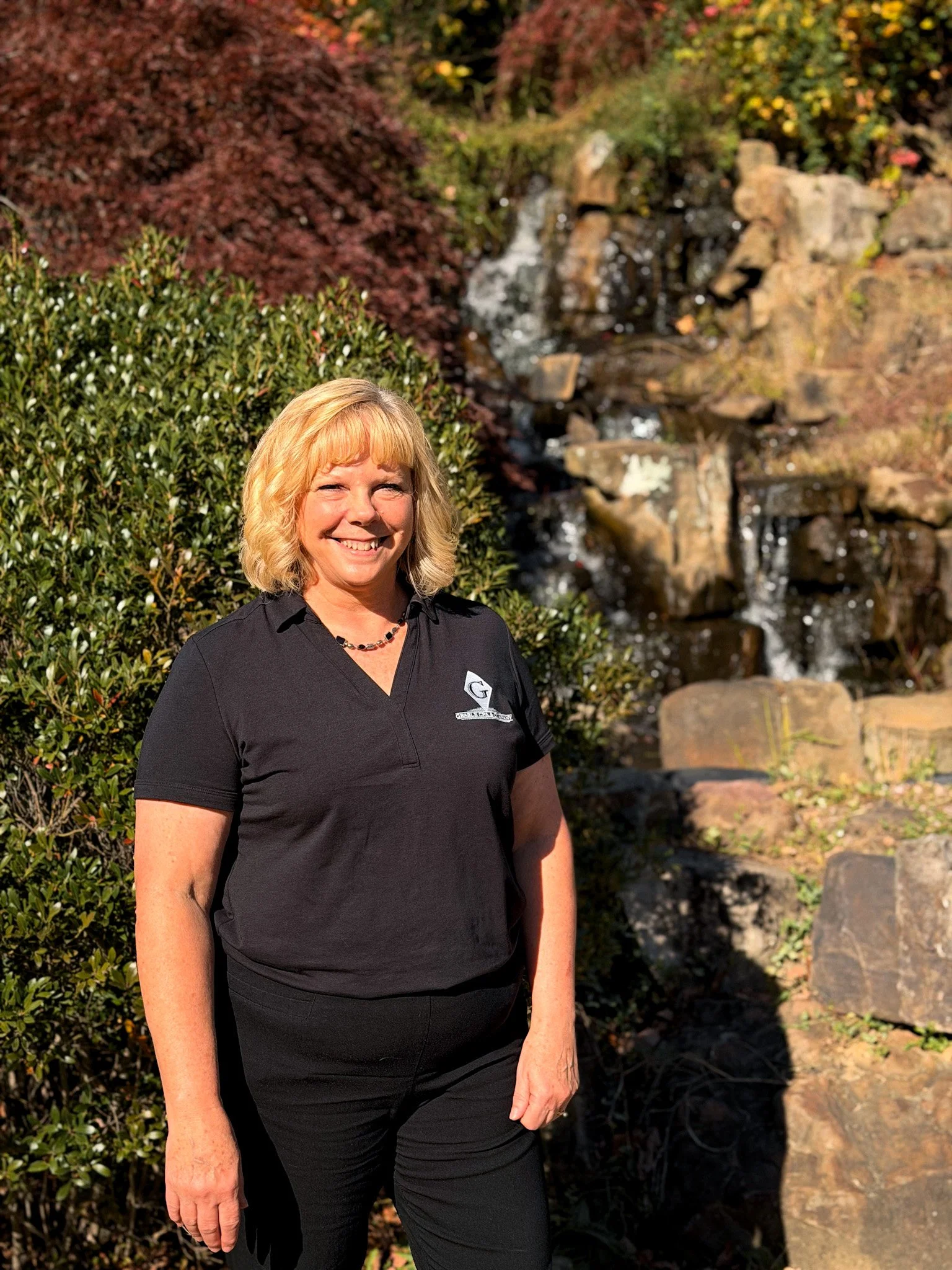 A woman with blonde hair smiling, standing in front of a wooden door, wearing a striped sweater and a long necklace. There is a sign on the door that reads 'Cody L. Grable, CPA'.
