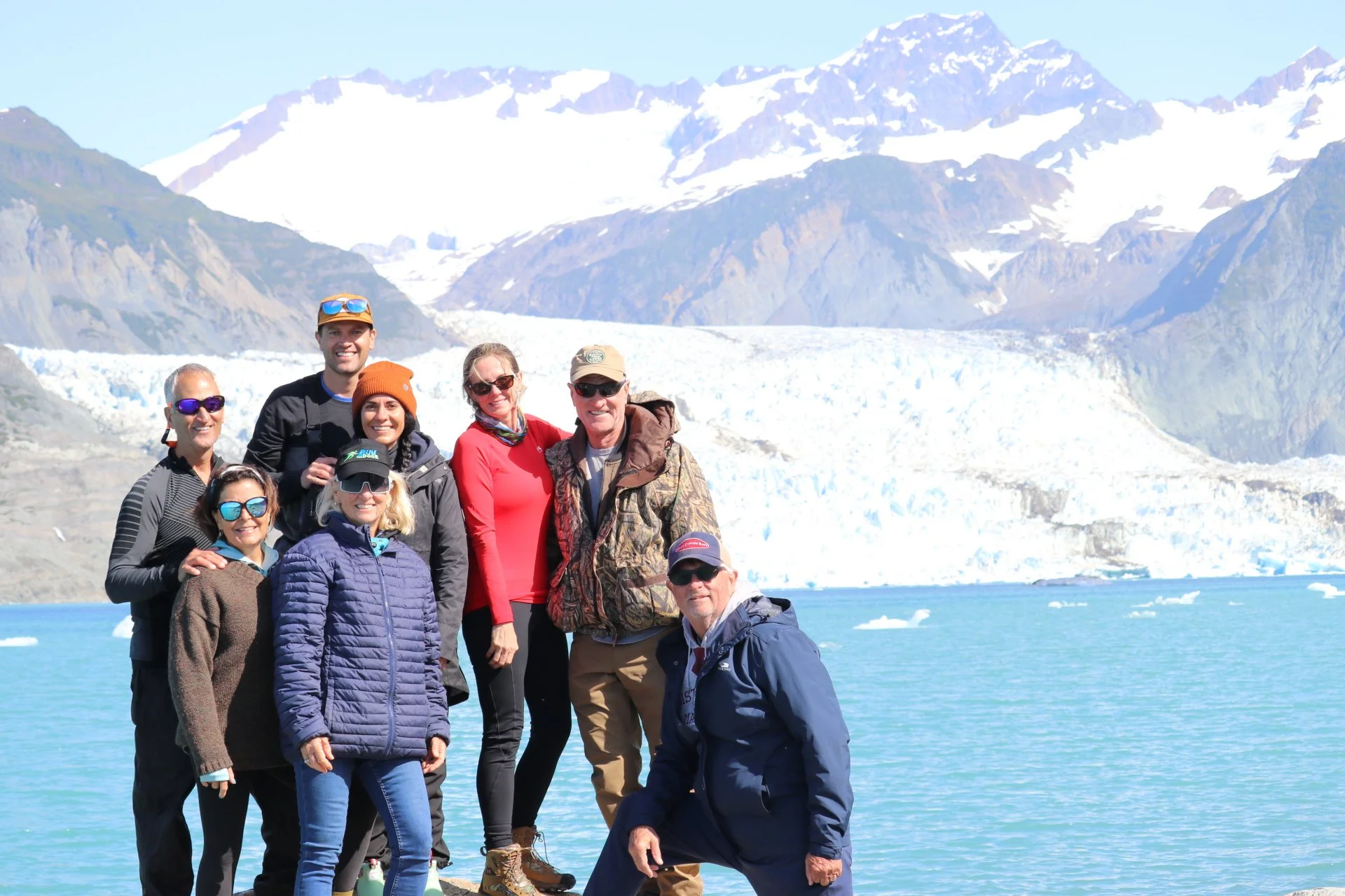 Hunter in camouflage clothing holding a rifle and ducks, standing in a grassy field at sunrise.