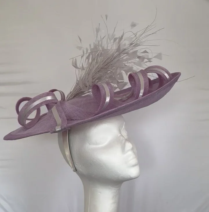 I have this absolutely gorgeous lavender coloured sinamay hat trimmed with pale silver feathers and sinamay swirls accented with silver satin available. This is a one-off design and will not be recreated. 

The hat is called LaVanda and she would be 