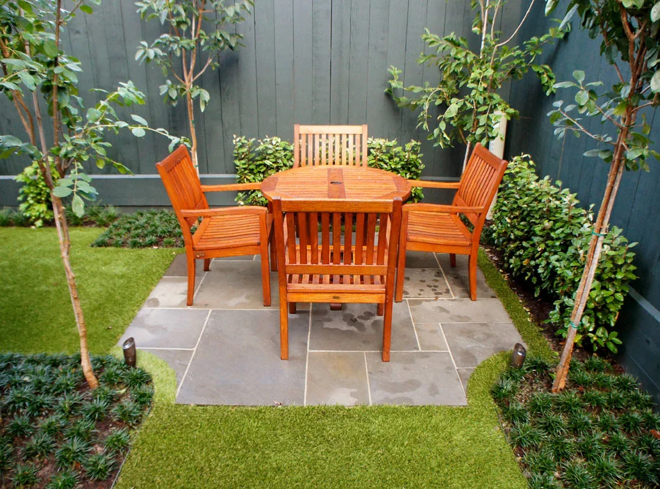 Pennsylvania Blue Flagstone was used to create this scalloped-edge patio with elongated Chinese Fringe Trees anchoring the four corners. The furniture is refinished teak and fits perfectly in this focal outdoor dining space.