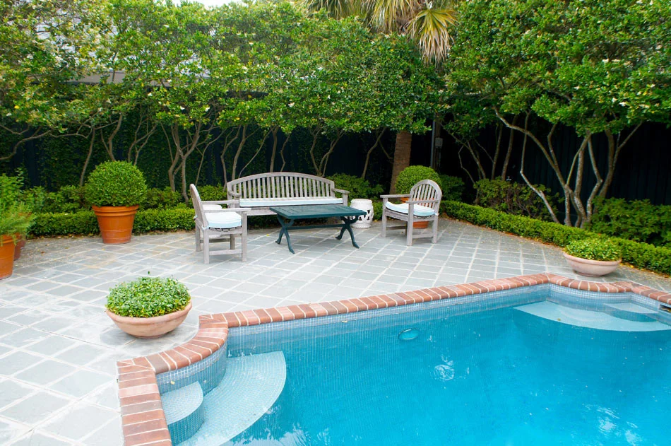 Terra cotta bowls of asian jasmine anchor the corners of the pool. Blue and white striped cushions are found throughout patio furniture and poolside lounges, giving the setting an english country feel.