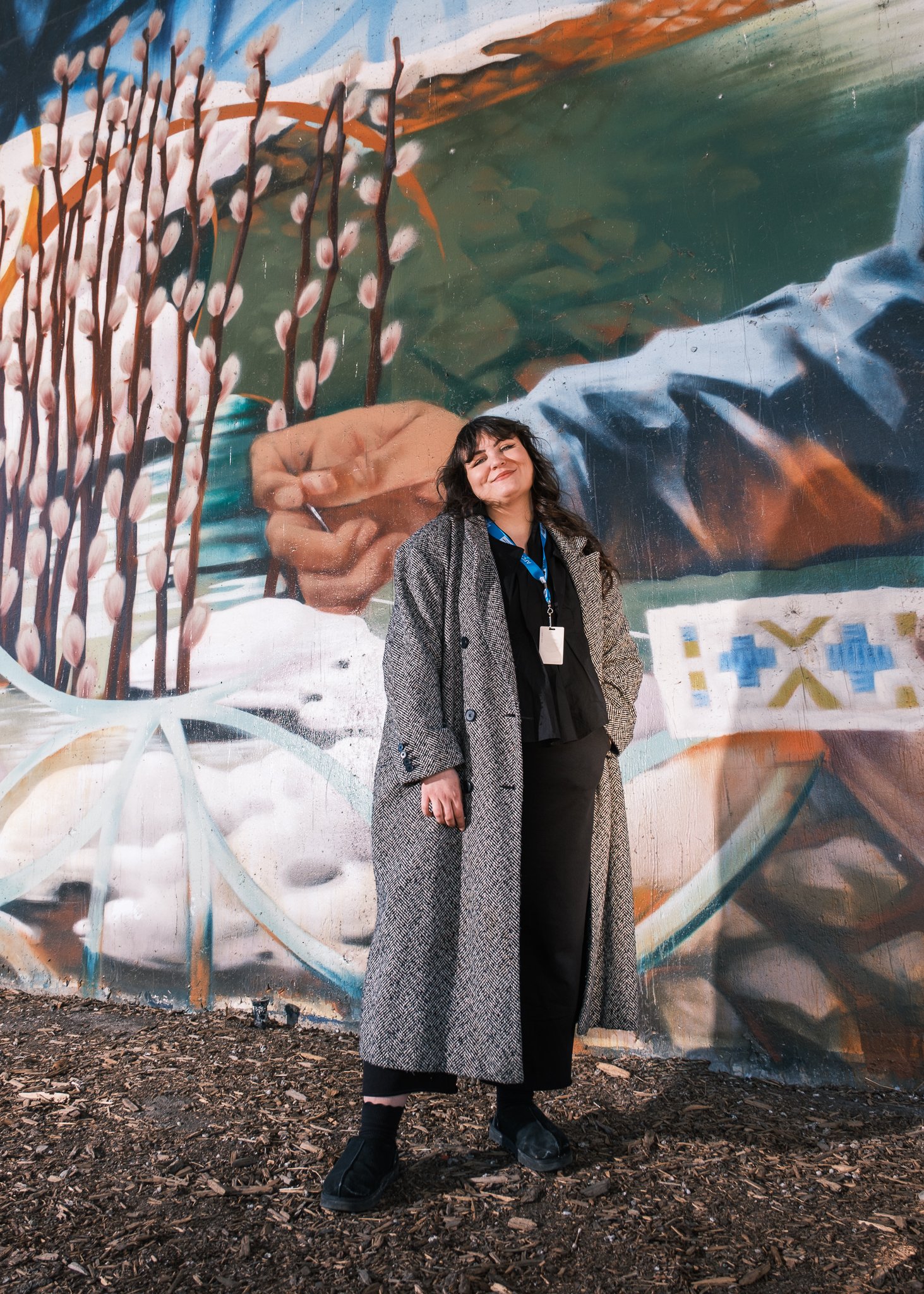 Bailey Dodds, Status Card and Registration Specialist for the Aboriginal Friendship Centre, stands in front of a mural in East Village Calgary.