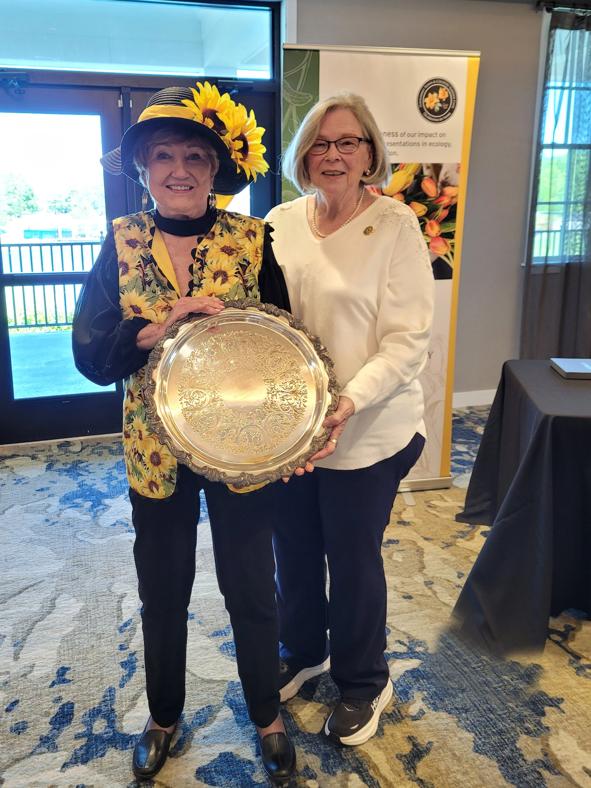 Barbara accepts an award from Jane for outstanding work at the Flower Show.