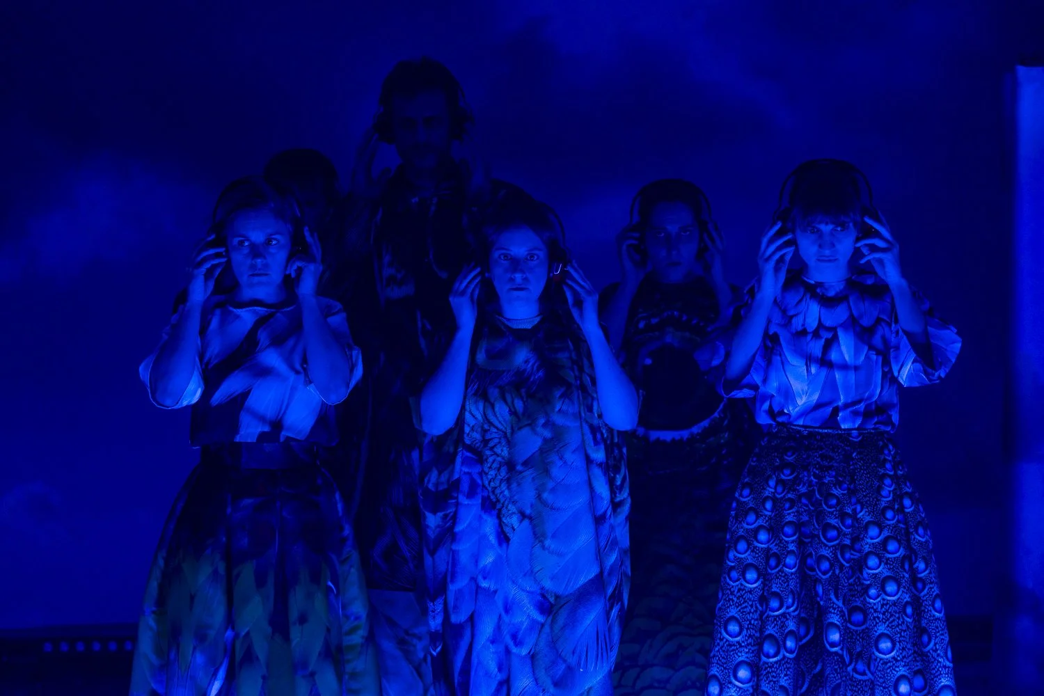 Cinco crianças com roupas coloridas, usando fones de ouvido, em um ambiente escuro com iluminação azul.