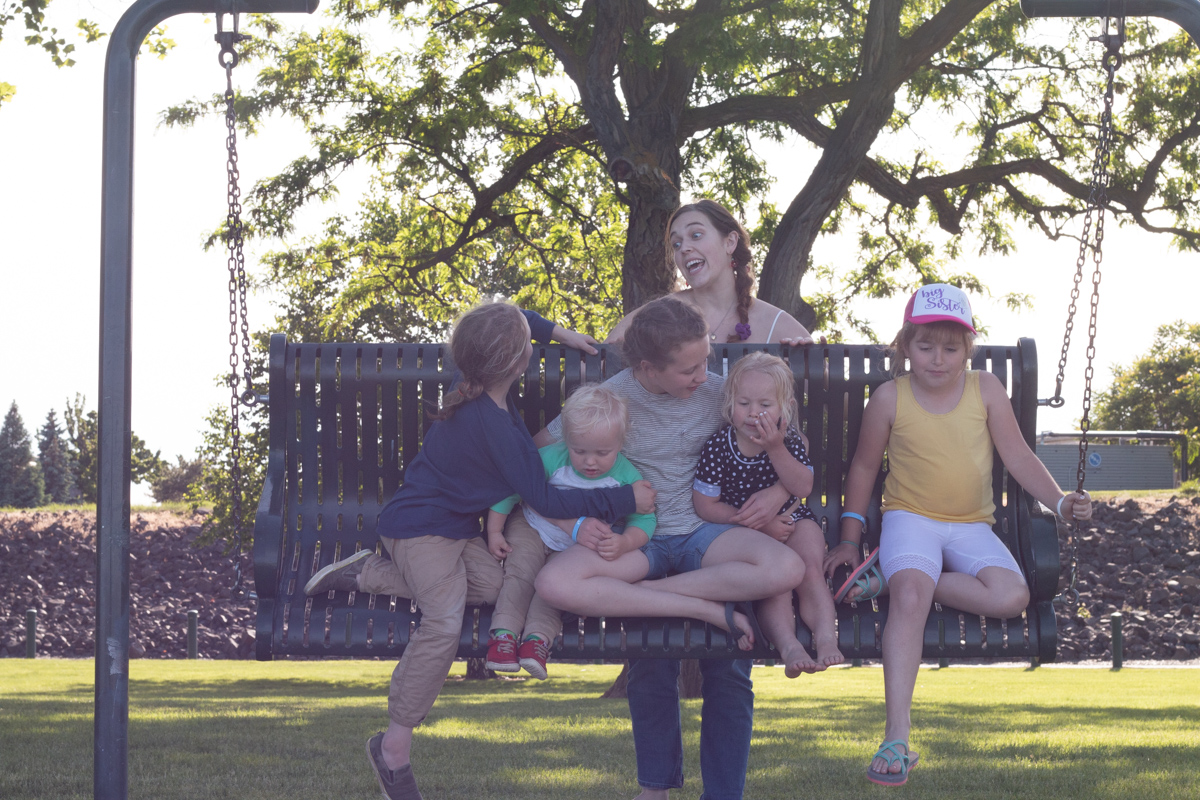 Boy sitting with friends on a swing in a park.