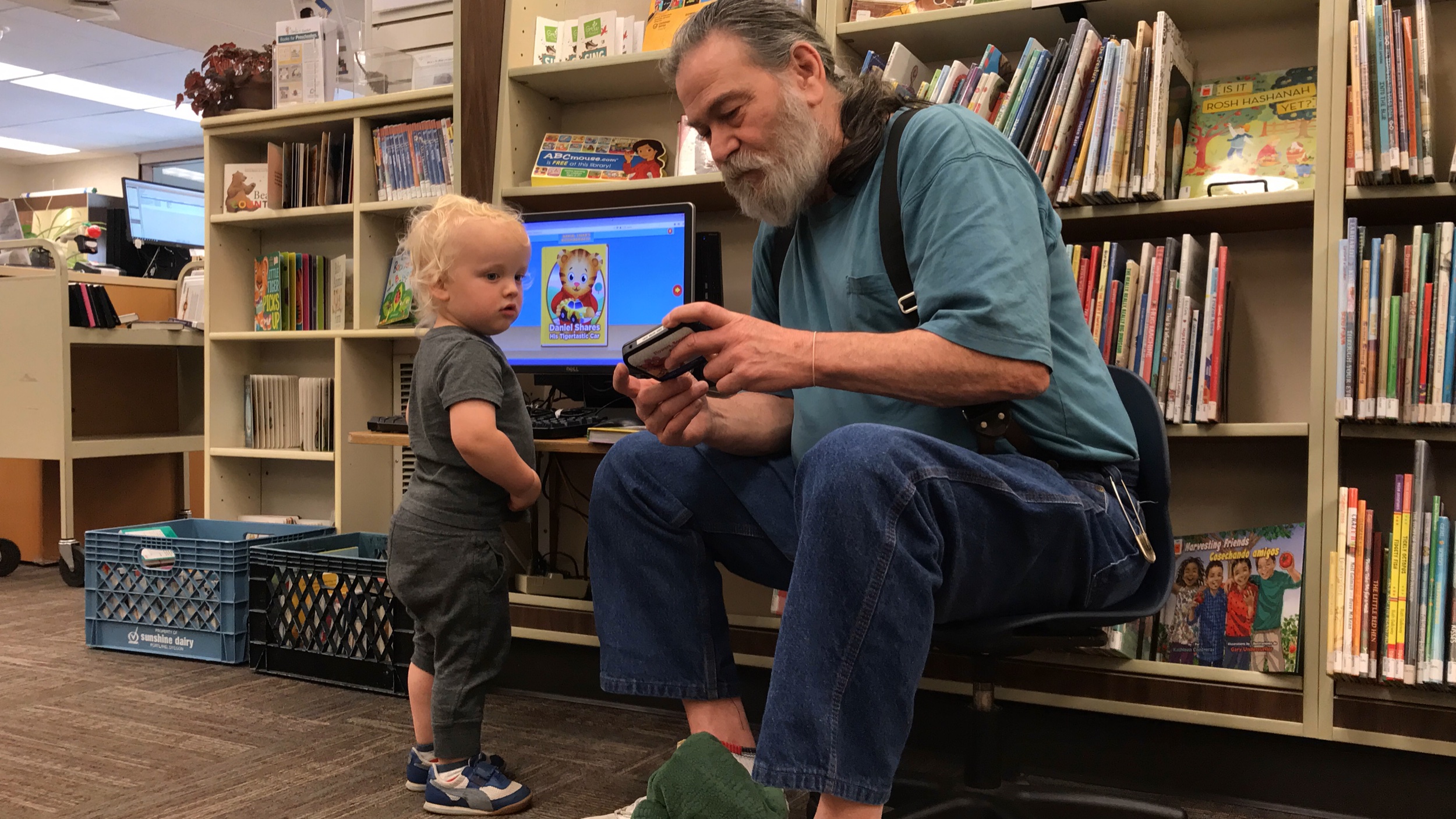 A Washougal Community Library worker with a burly beard assists a toddler-age male patron in the children’s section.