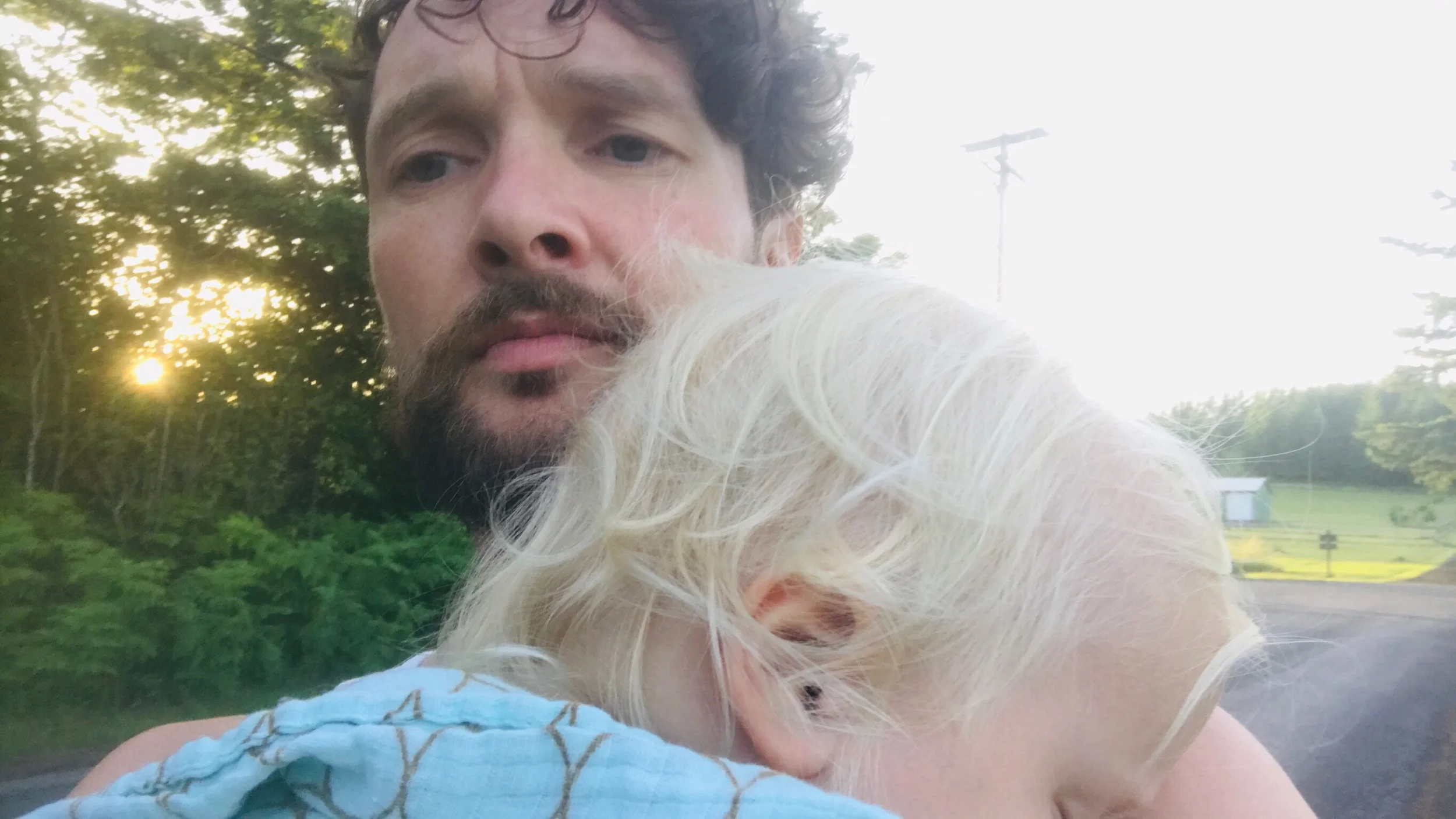 Dad taking summer evening walk while holding sleeping toddler