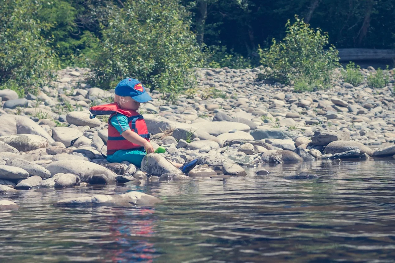 Toddler-age boy sitting on river bank playing with rocks.jpg