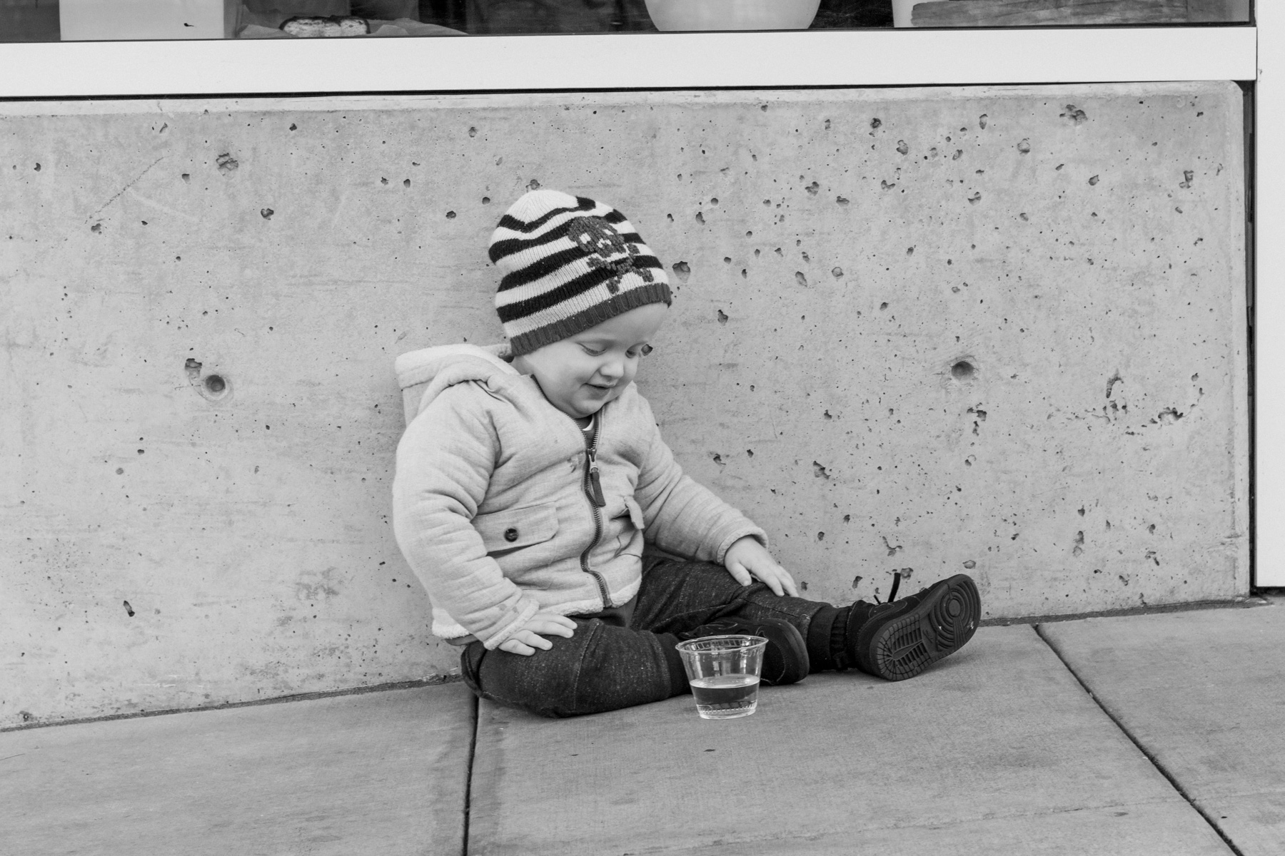 Twenty-four month old boy sitting on city sidewalk.