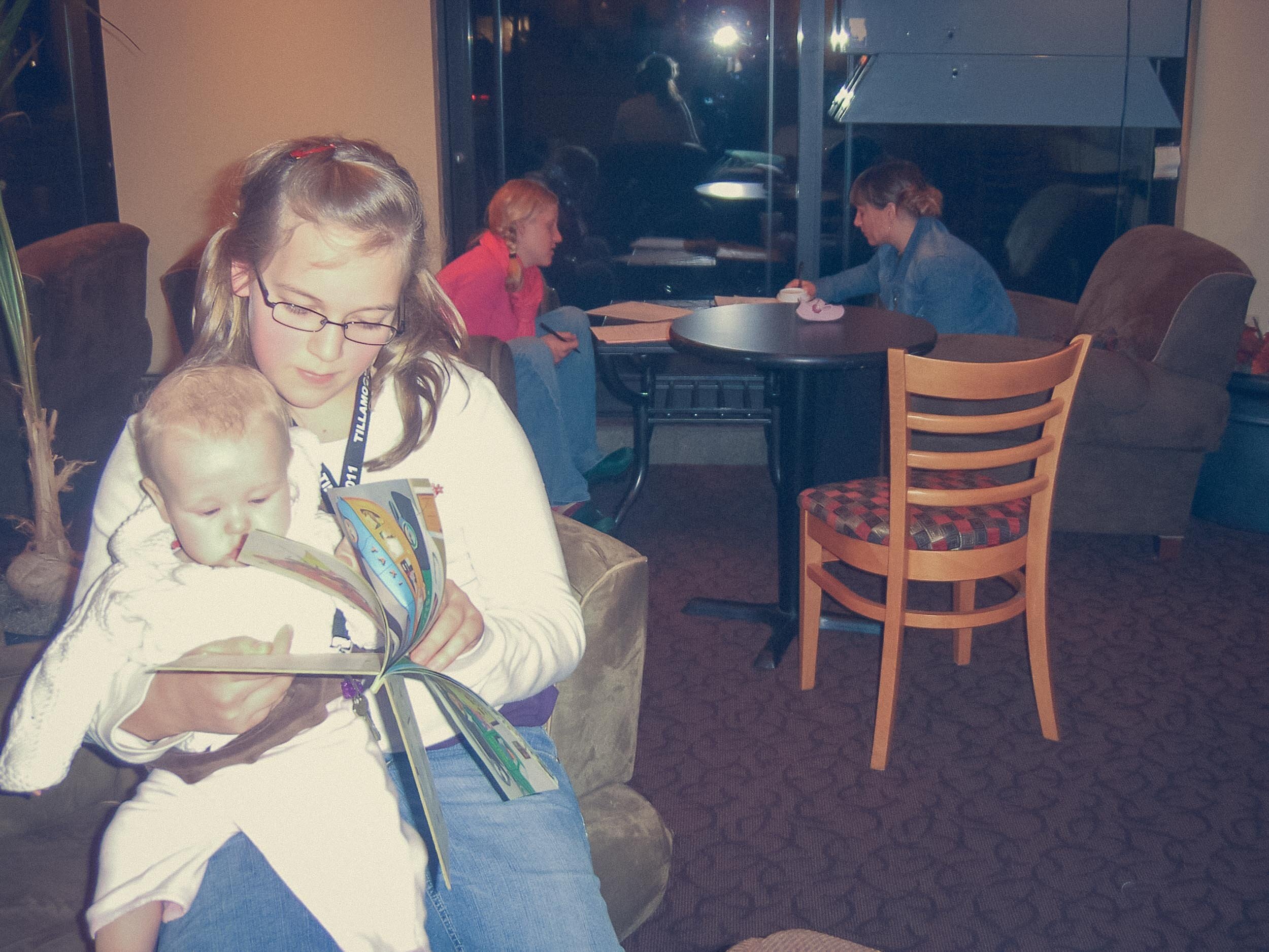 Teenage girl reading to a young girl in a coffee shop.