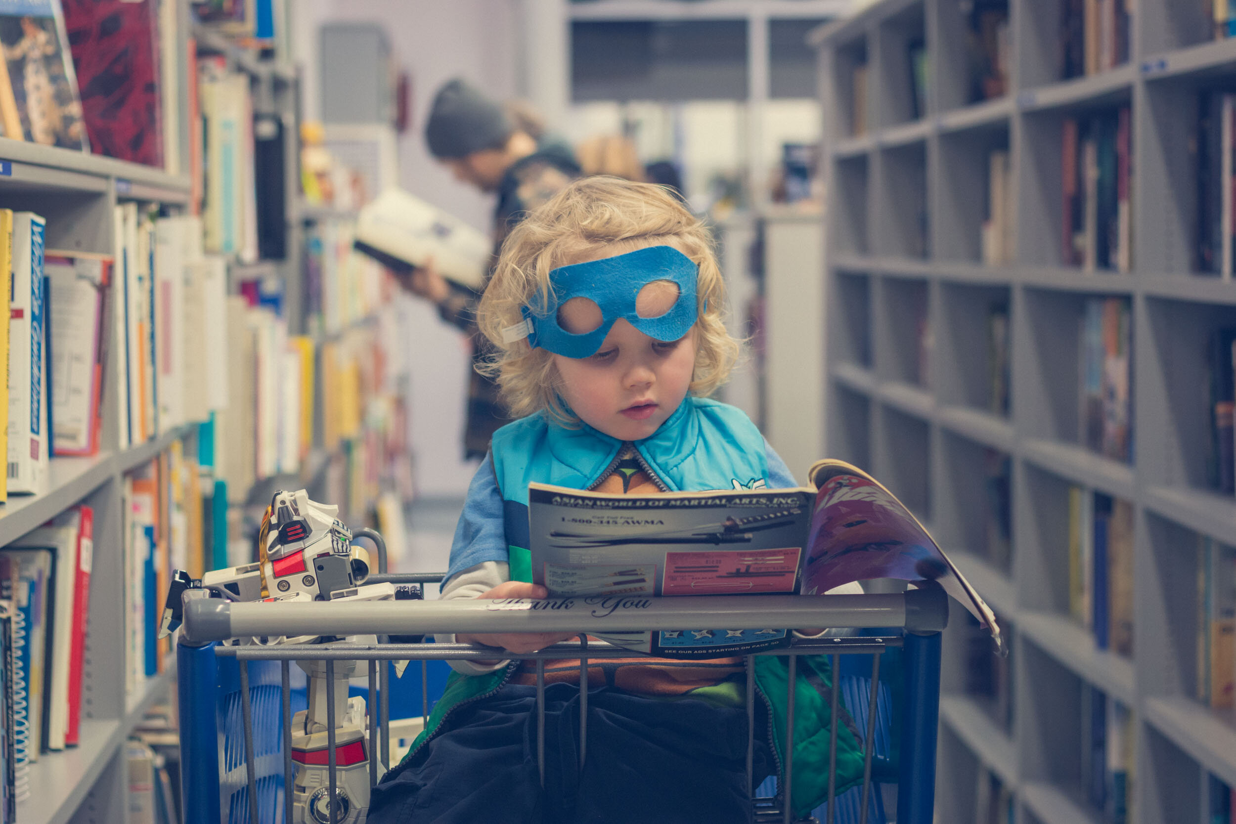 Four-year old boy sitting in shopping cart reading a book.