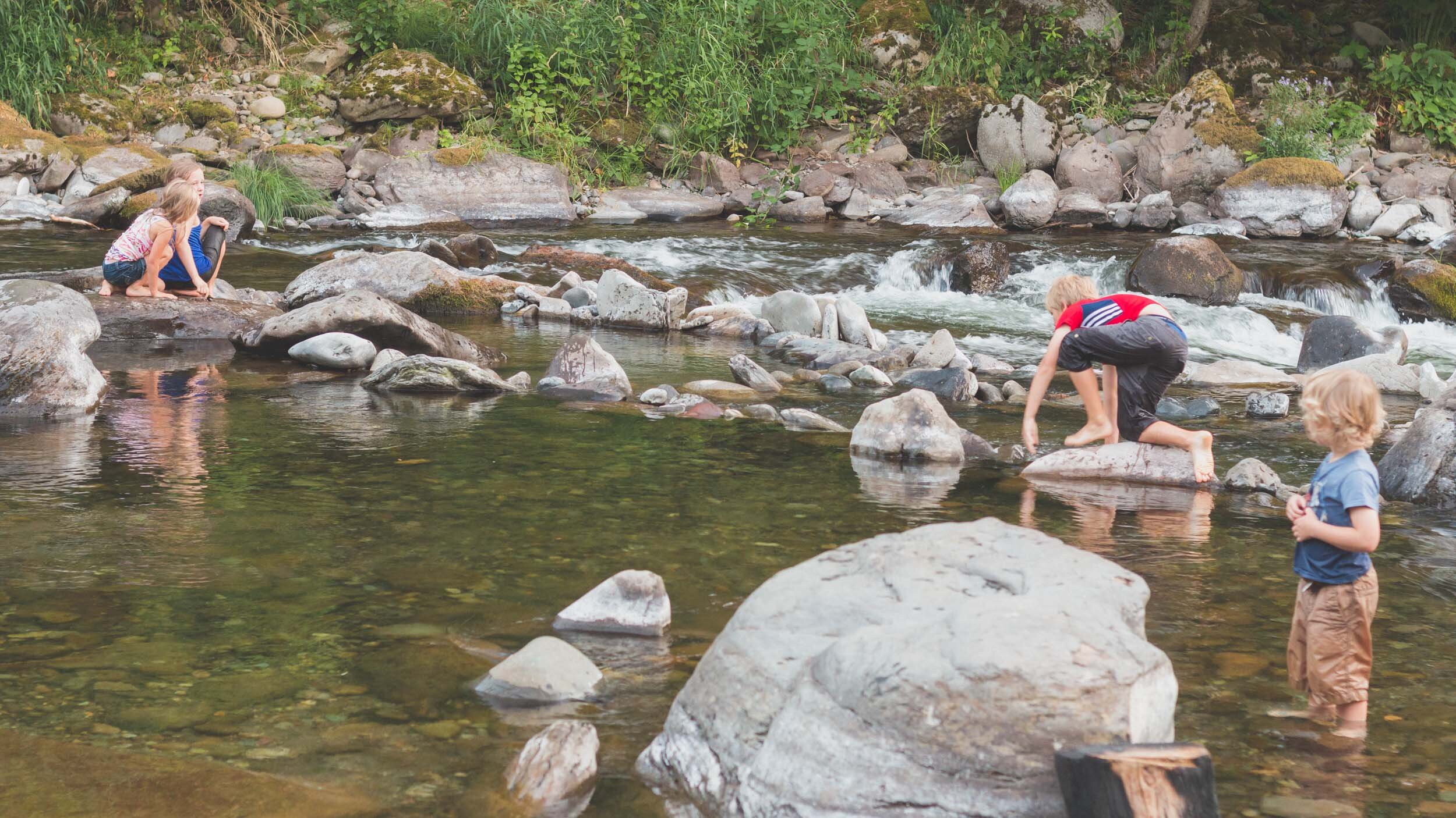 Four children play in and explore a river on a quiet Shabbat evening